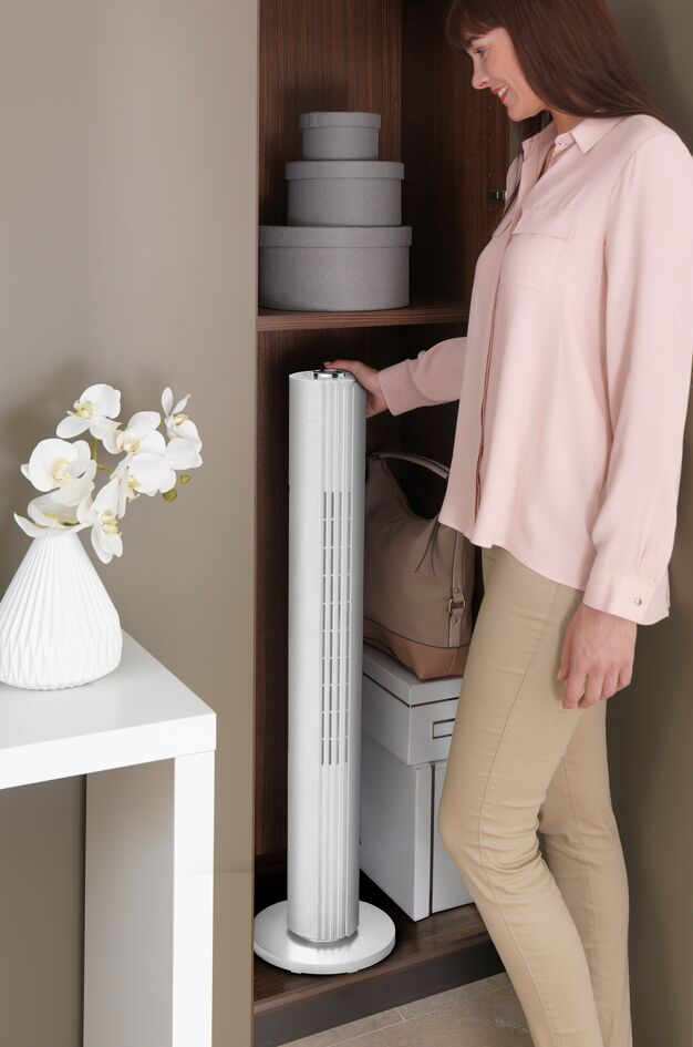 A woman is putting a white fan into a cabinet, next to some boxes and a handbag.
