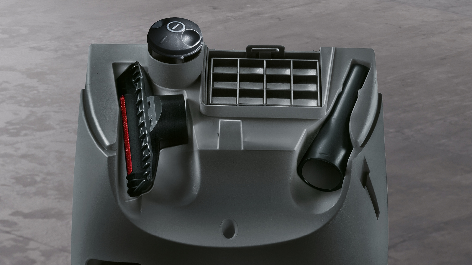 Detail des Zubehörfachs eines grauen Staubsaugers. Enthält Bürsten und ein Fugendüse.