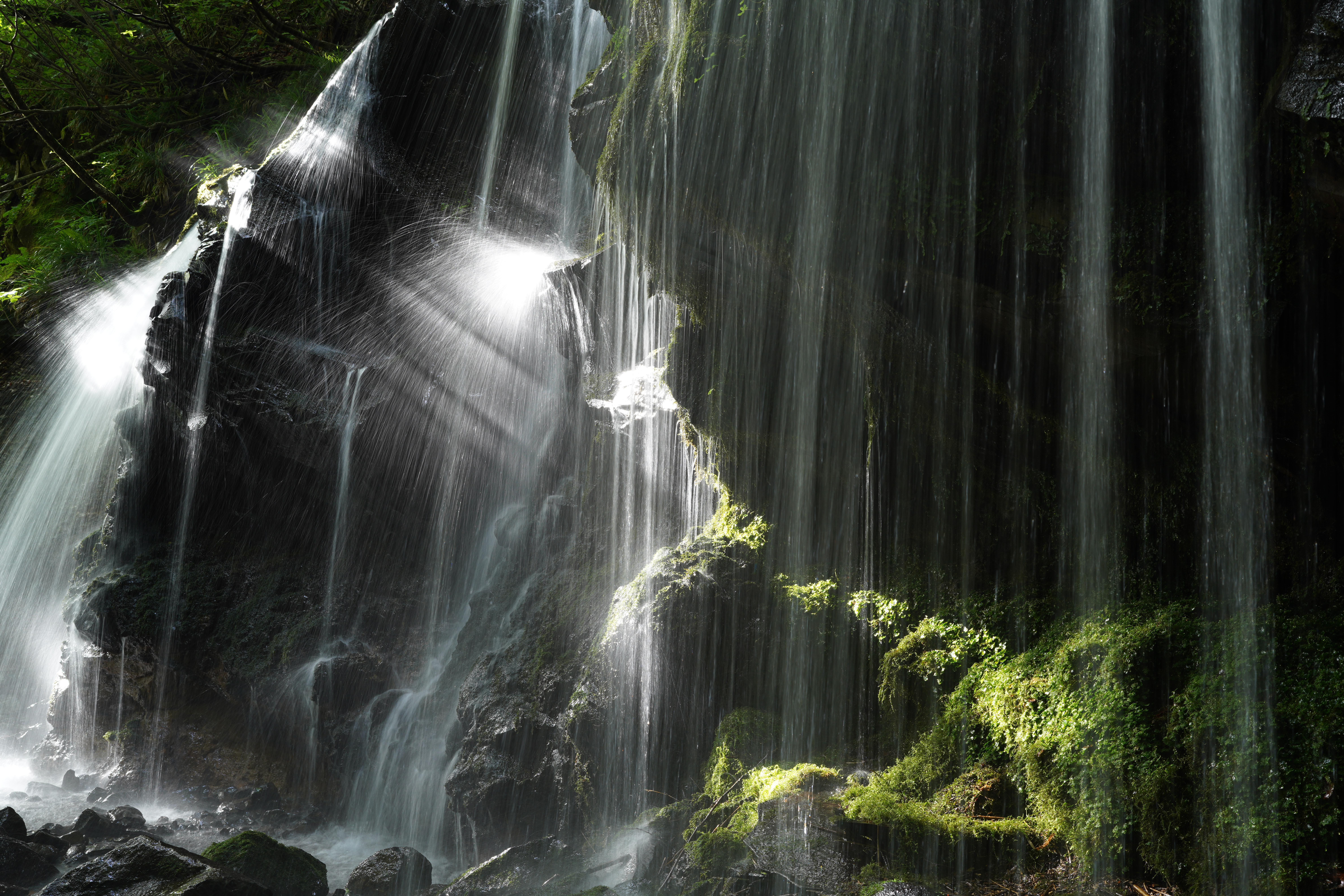 Wasserfall mit über Felsen und Moos stürzendem Wasser. Sonnenlicht scheint durch das fallende Wasser.