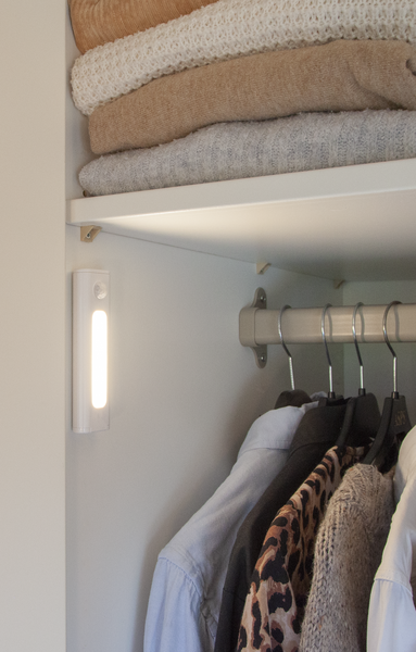 All'interno di un armadio, maglioni impilati sopra camicie appese, una luce bianca illumina da un pannello laterale.