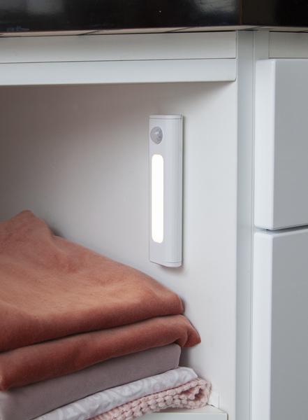 Luce LED bianca all'interno di un armadio bianco. Una pila di coperte piegate davanti alla luce.