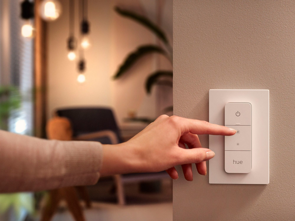 Mano presionando un botón en un interruptor de luz blanco montado en la pared junto a una pared.
