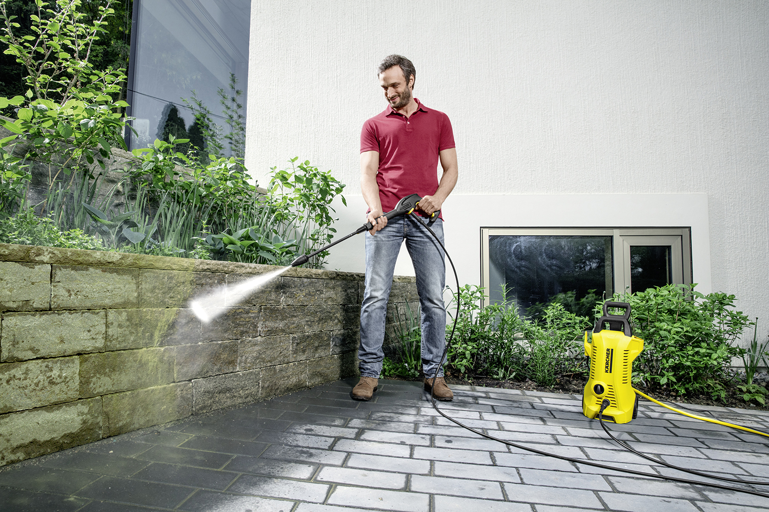 Homme lavant un mur en pierre avec un nettoyeur haute pression. Machine jaune et tuyau.