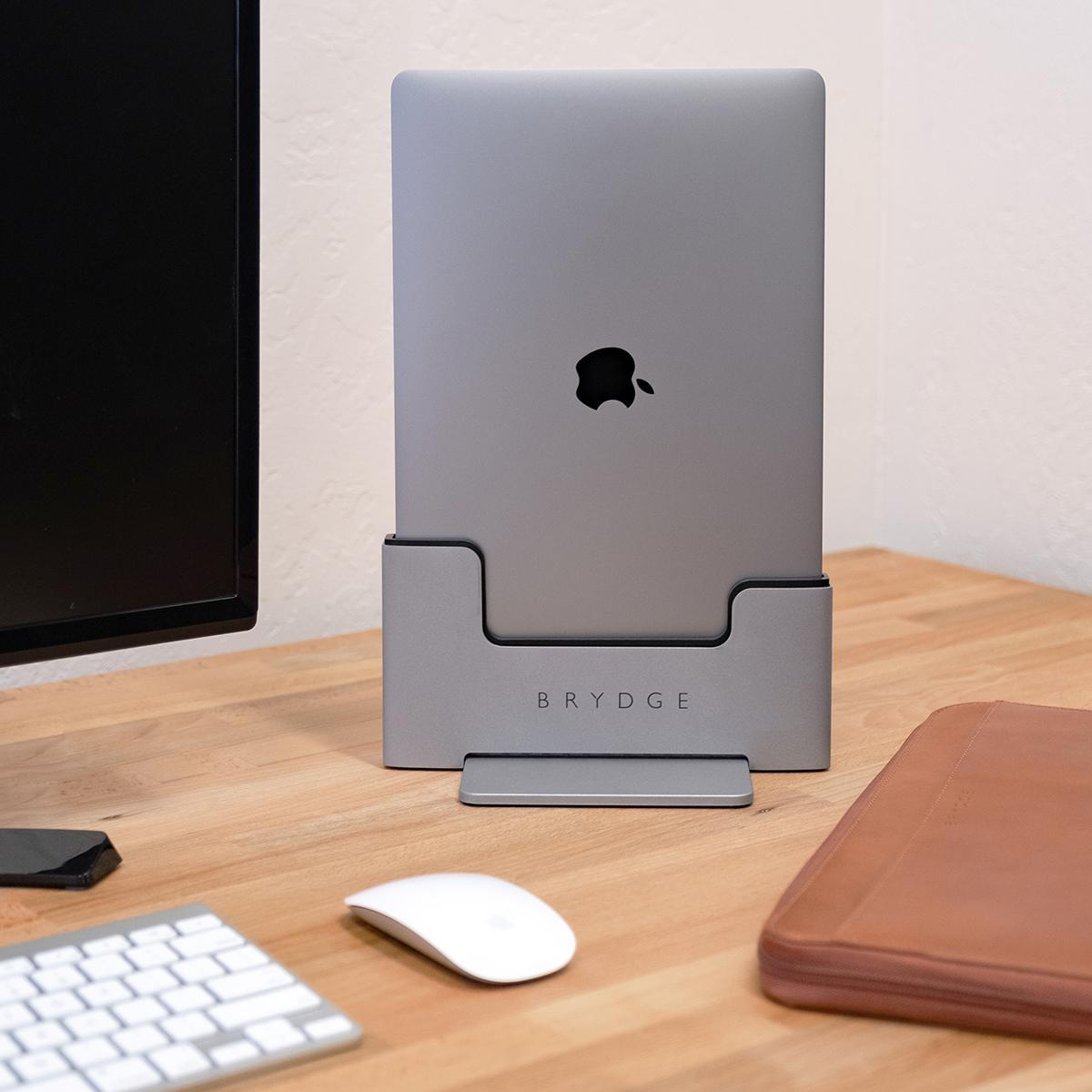 Ein graues Laptop in einem grauen Ständer auf einem Holzschreibtisch mit Tastatur und Maus.