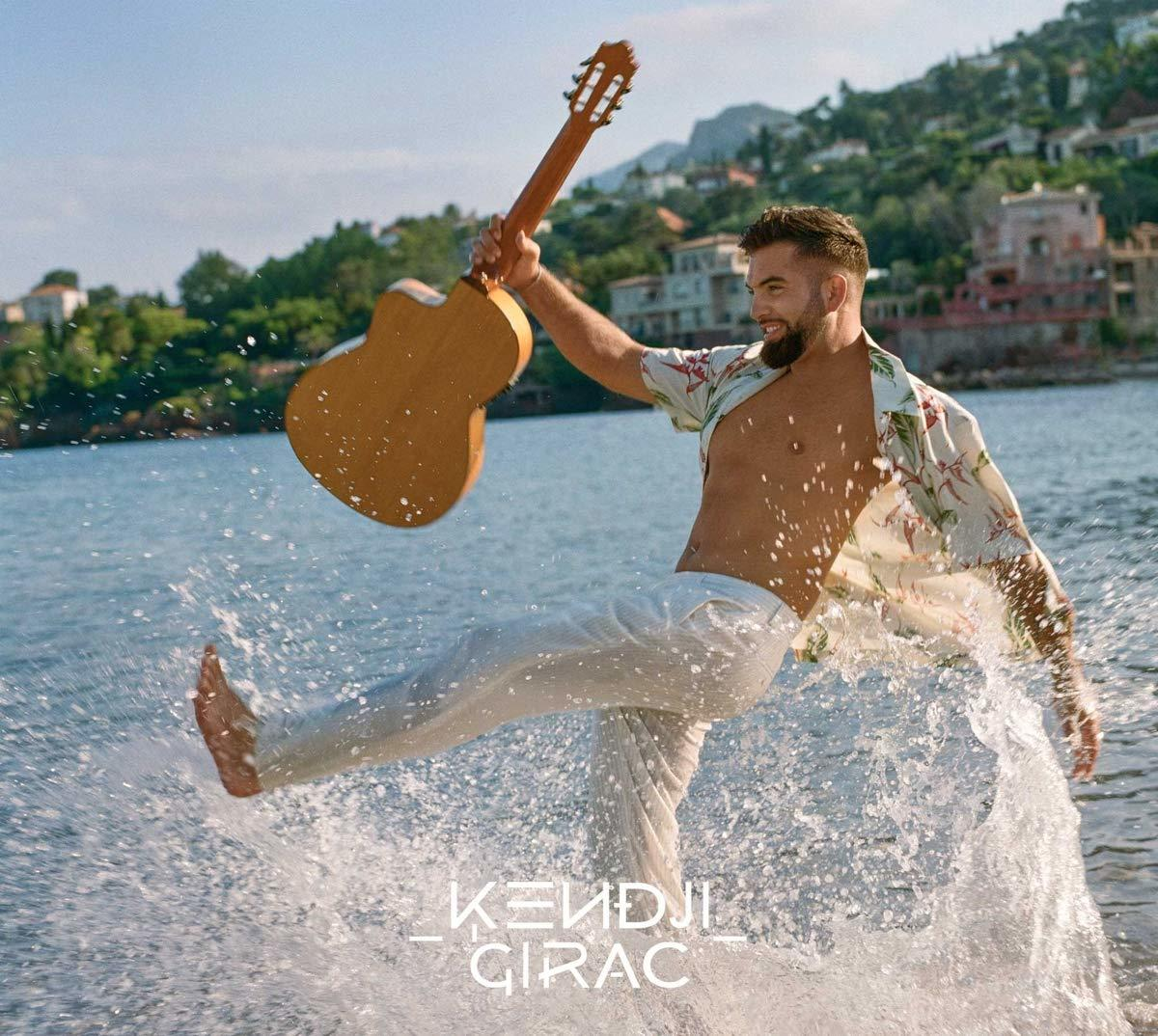 Homme dans l'eau tenant une guitare. Il porte une chemise fleurie et un pantalon blanc, l'eau éclabousse.