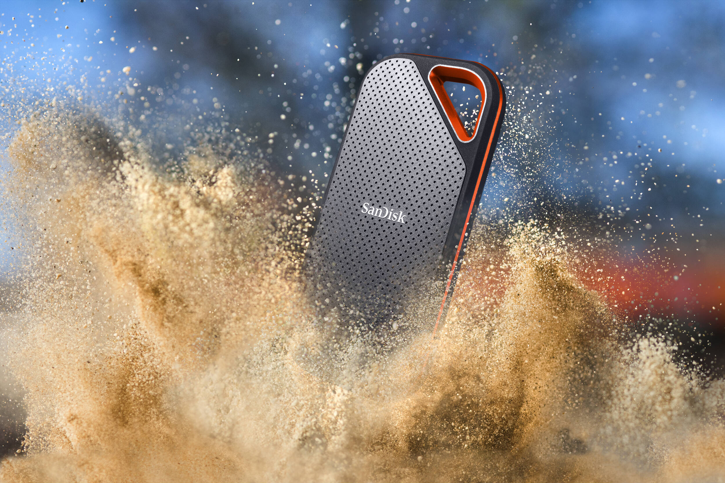 Eine schwarze und orangefarbene SanDisk externe Festplatte mit Sand. Verschwommener Hintergrund.