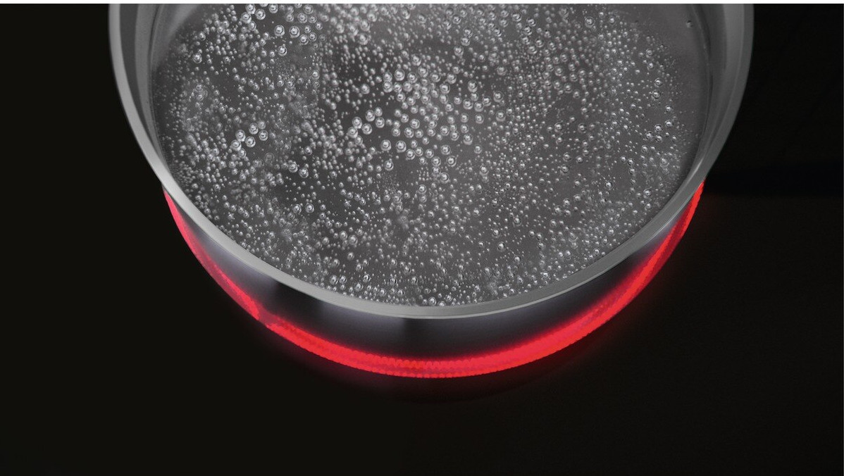 Close up of a pot with boiling water on a black cooktop, glowing red.