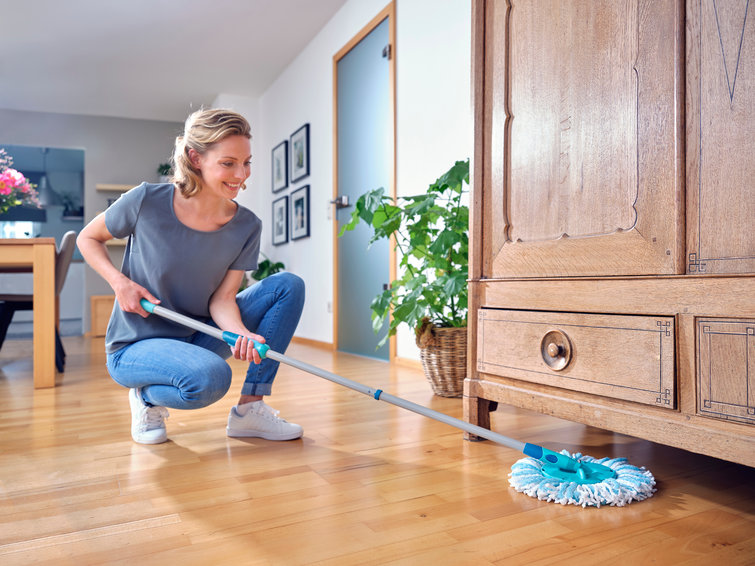 Vrouw dweilt houten vloer. Ze glimlacht, de vloer heeft houtpatronen.