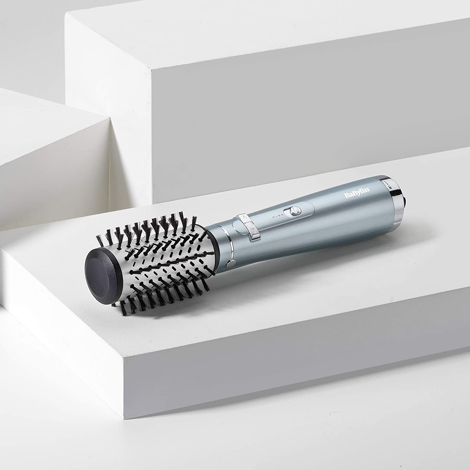 Brosse à coiffer bleu clair sur un bloc blanc. La brosse a des poils noirs et un manche argenté.