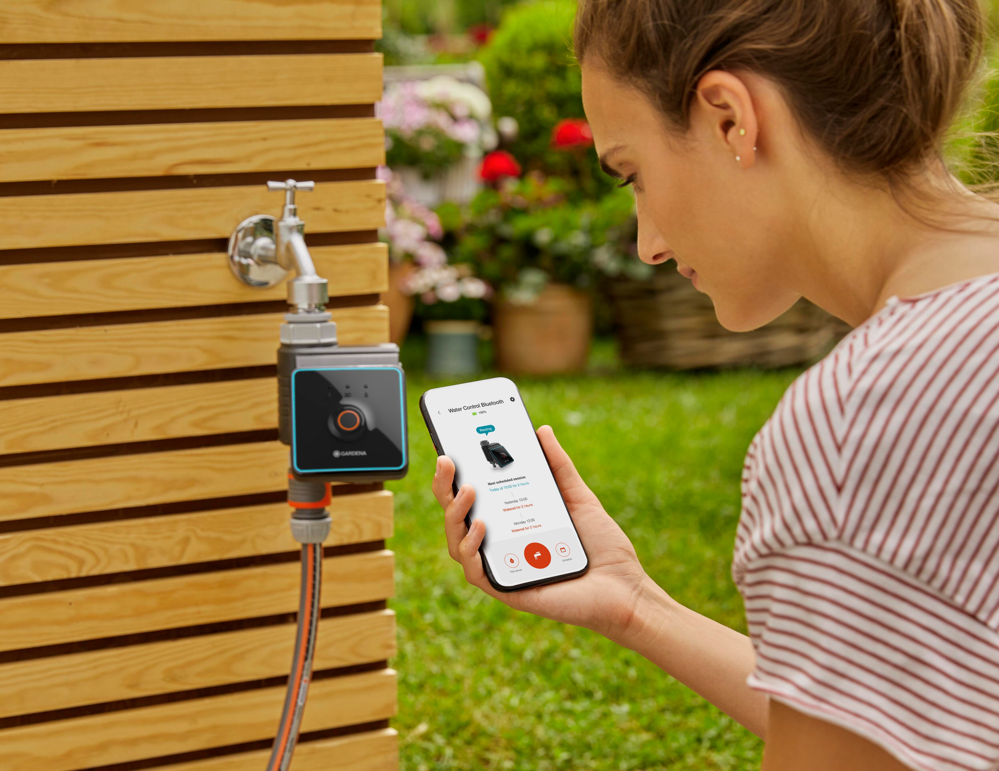 Frau benutzt Smartphone neben einem an der Wand montierten Wassersteuergerät.