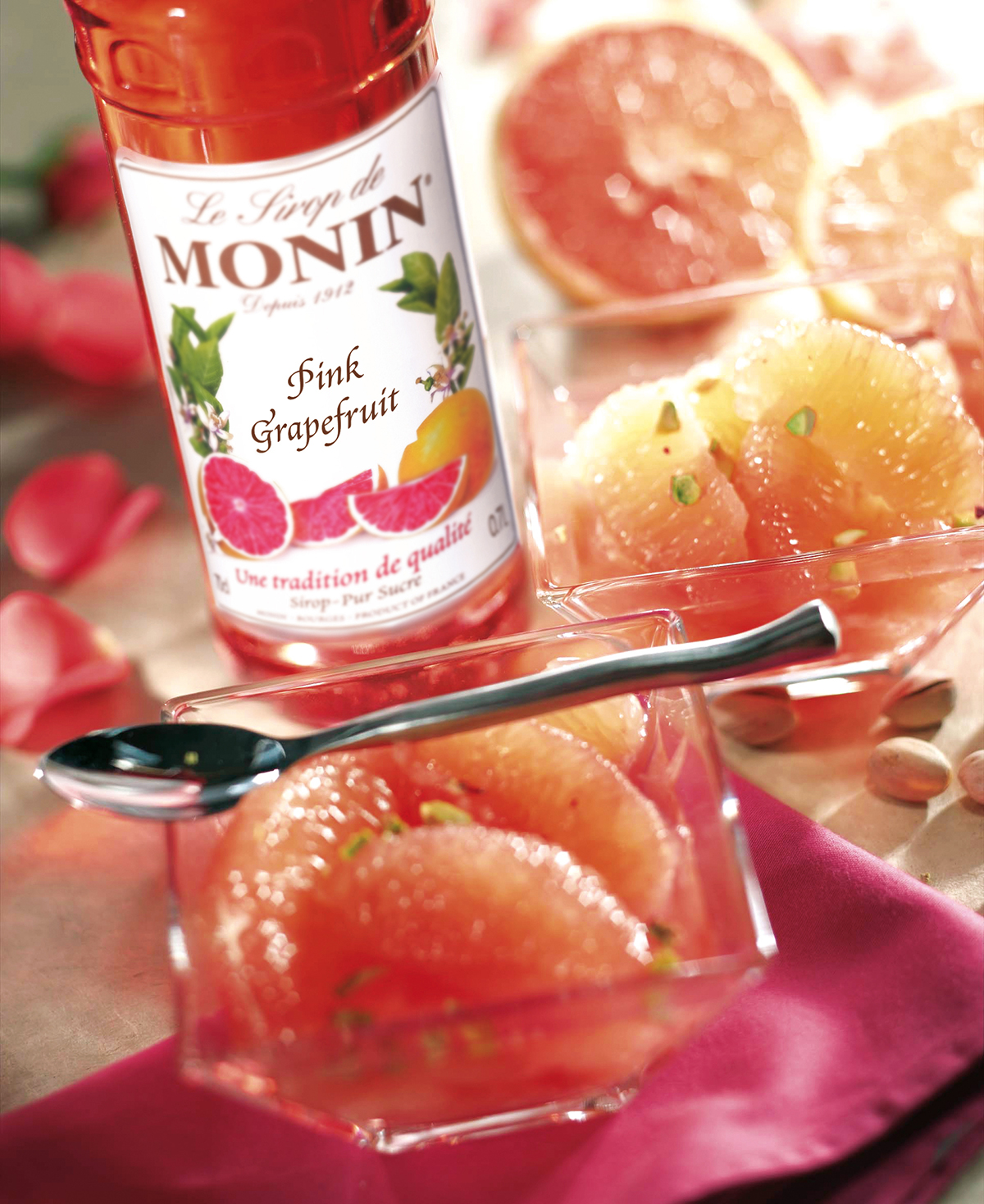 Pinke Grapefruitscheiben in kleinen Glasschalen mit Sirup und einer Flasche rosa Grapefruitsirup.