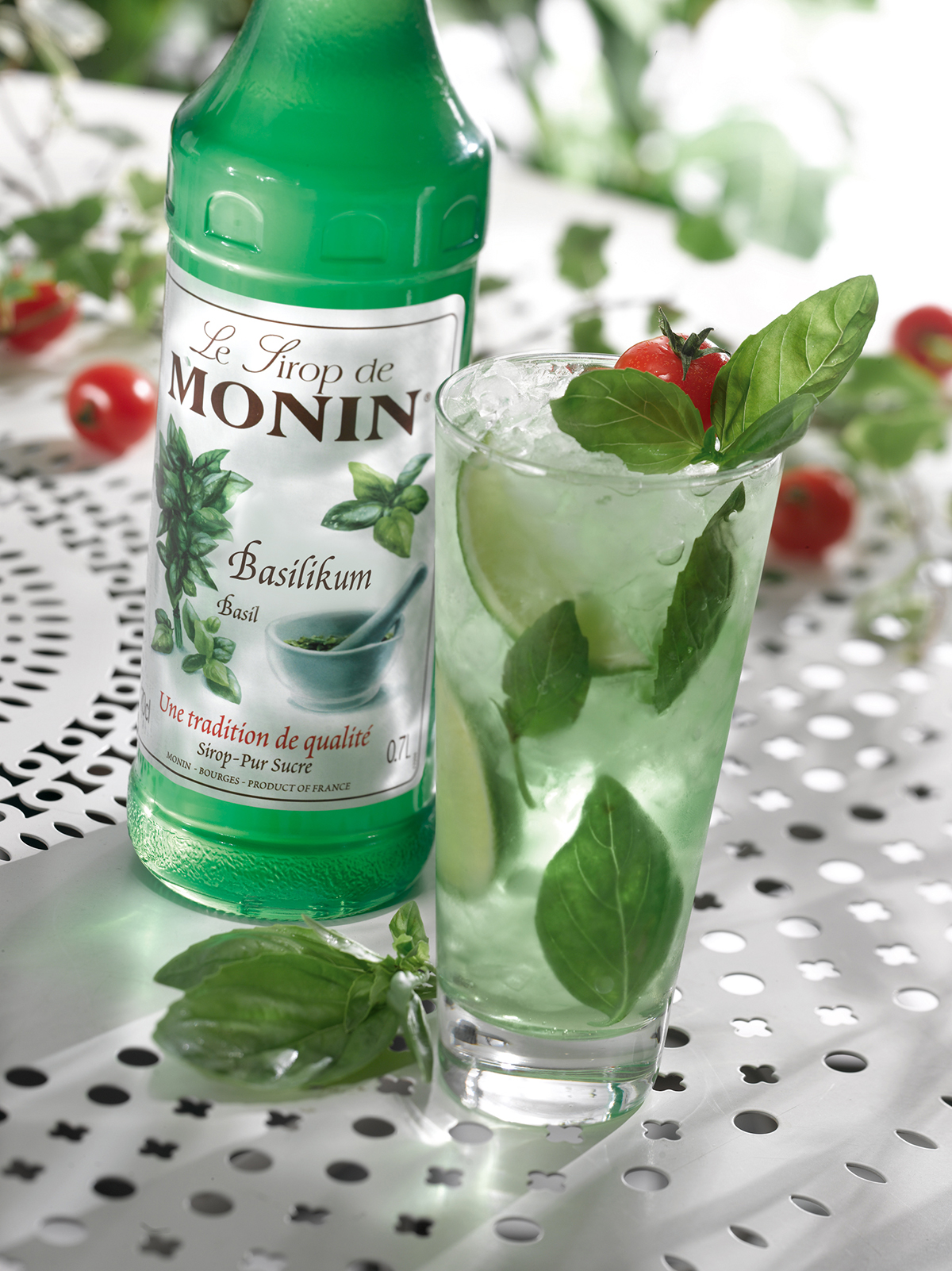 Basilikum-Cocktail mit Monin-Basilikum-Sirup-Flasche und Tomaten, Basilikum-Blätter-Garnitur.