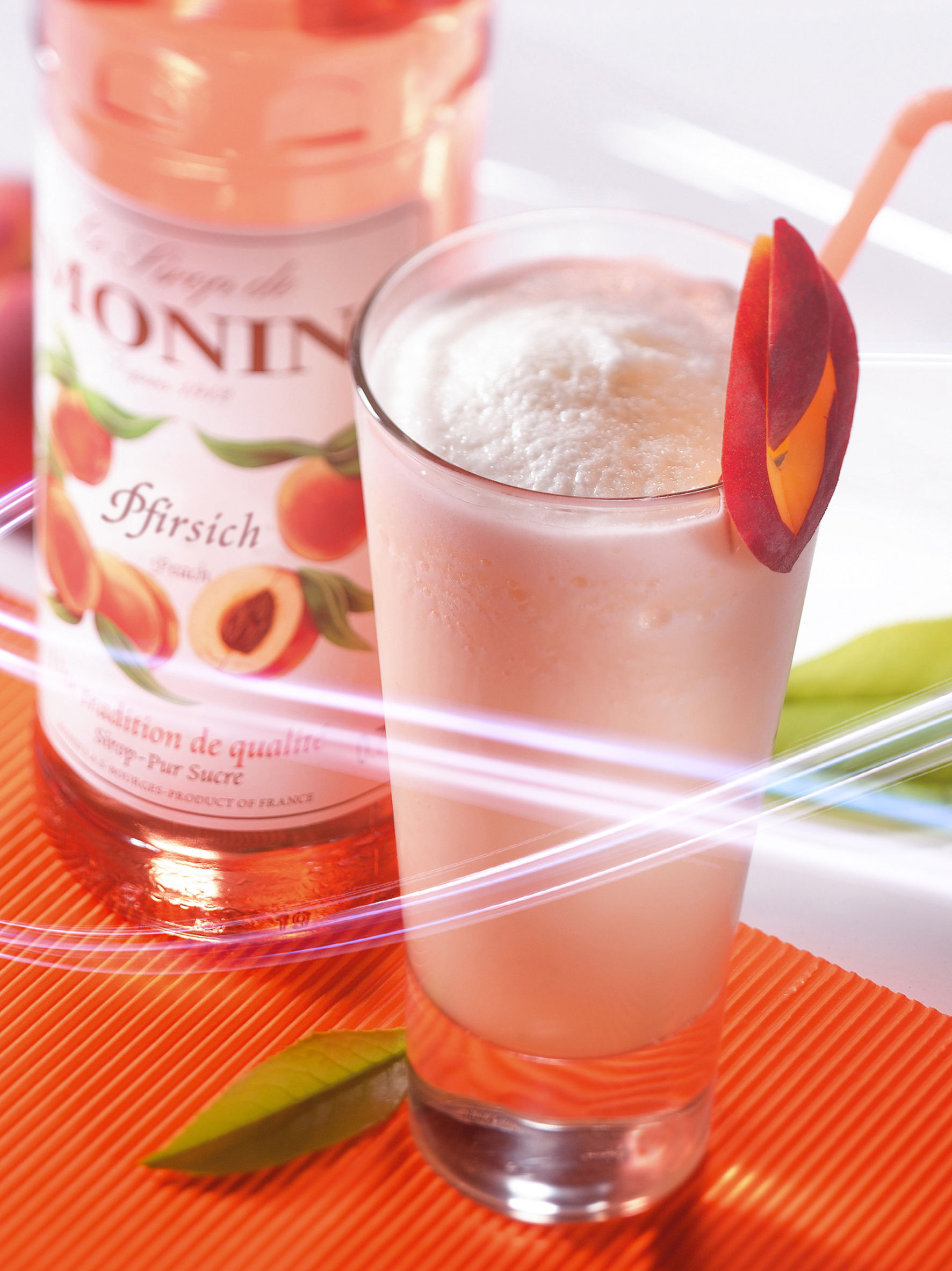Ein Pfirsich-Smoothie mit einem Pfirsichscheiben-Belag und einer Flasche Pfirsichsirup.