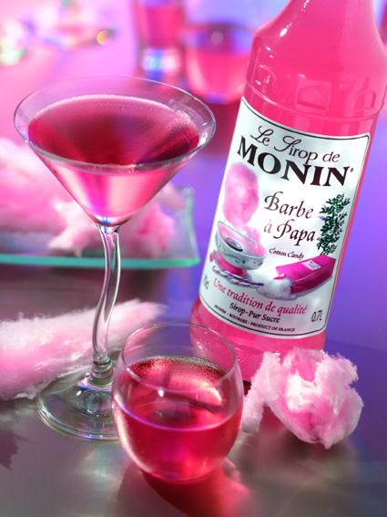 Ein rosa Getränk in einem Martiniglas und einem kleinen Glas. Zuckerwatte und eine Flasche sind in der Nähe.