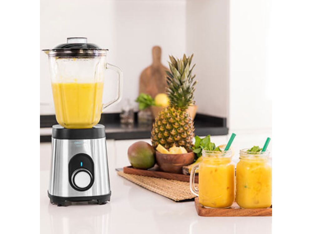 Una licuadora con líquido amarillo, piña, mango y bebidas en frascos en una encimera de cocina.