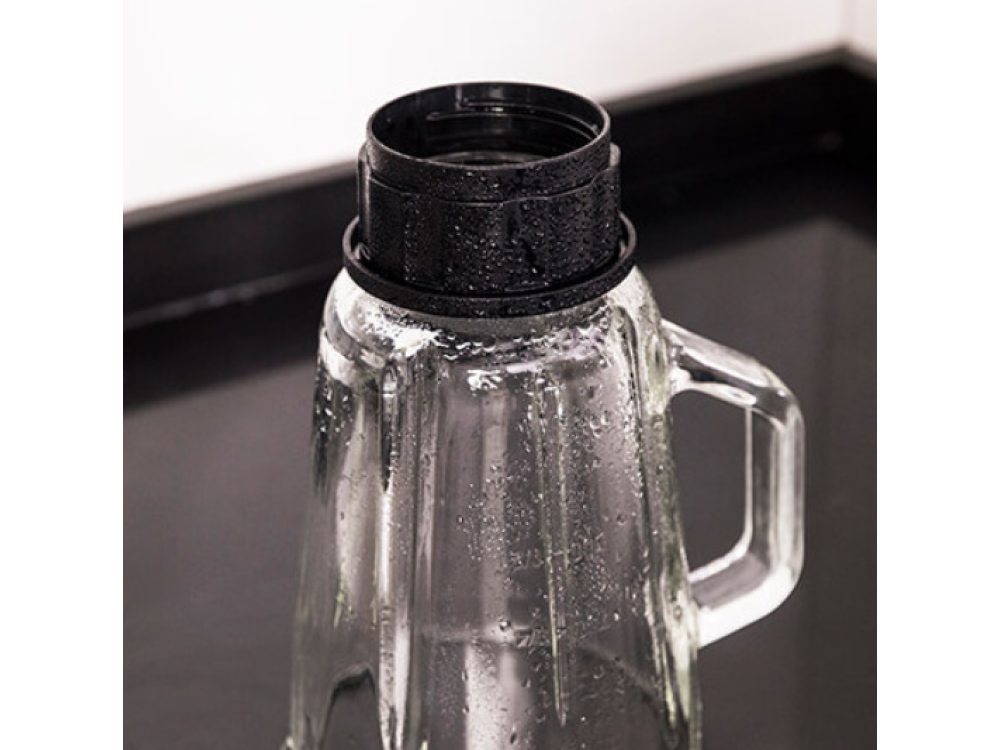Una jarra de cristal transparente con tapa negra. La jarra tiene un asa. Gotas de agua visibles en el vidrio y la tapa.