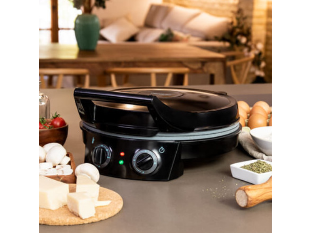 Máquina para hacer pizza negra sobre una mesa. Ingredientes como queso, tomates y huevos cerca. Una mesa de madera al fondo.