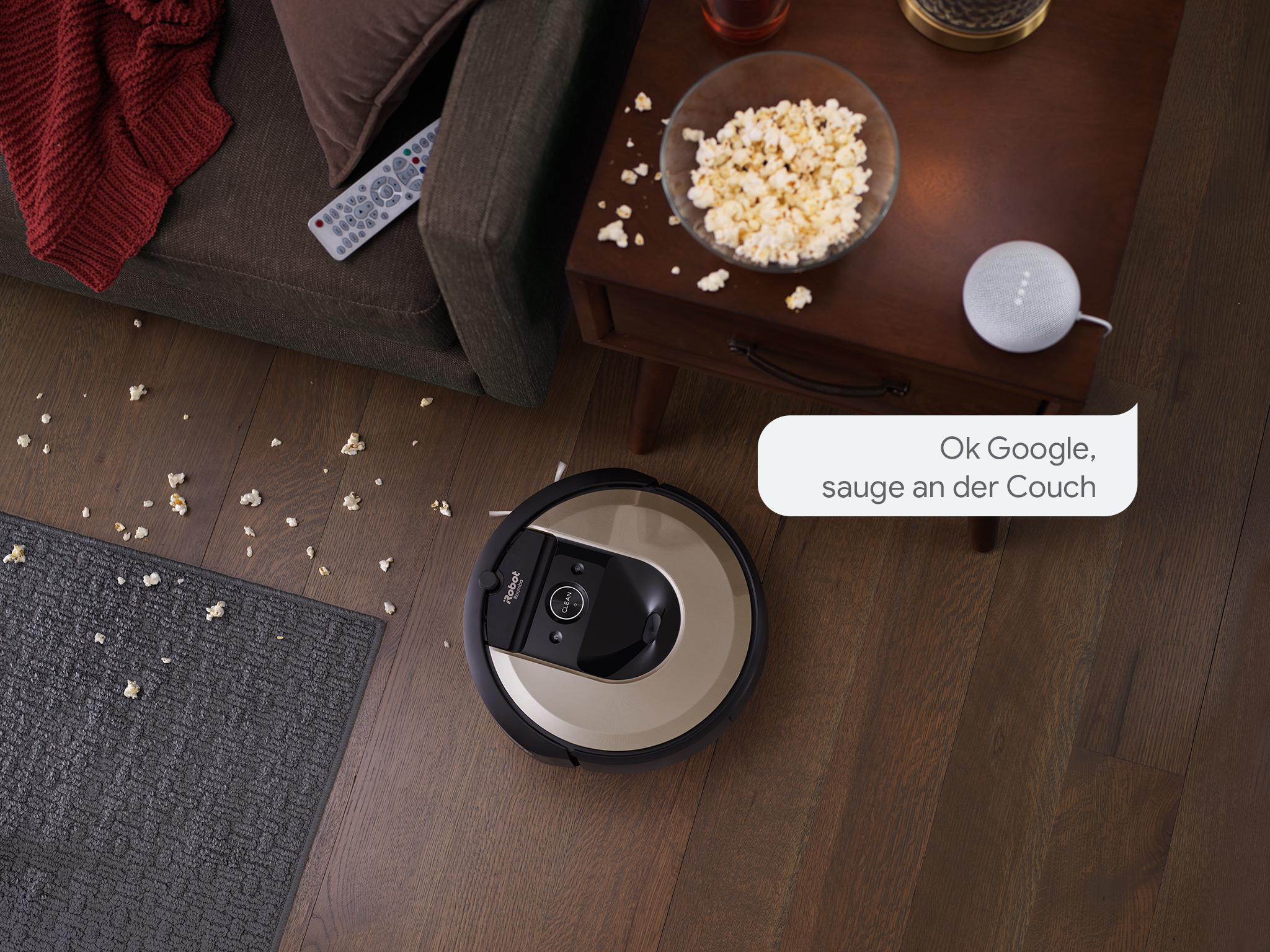 Roboter-Staubsauger auf Holzboden, mit verschüttetem Popcorn und Google Home.