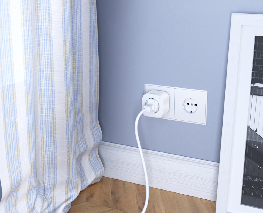 Ein Smart-Plug in einer Steckdose an einer blauen Wand. Links ein Vorhang.