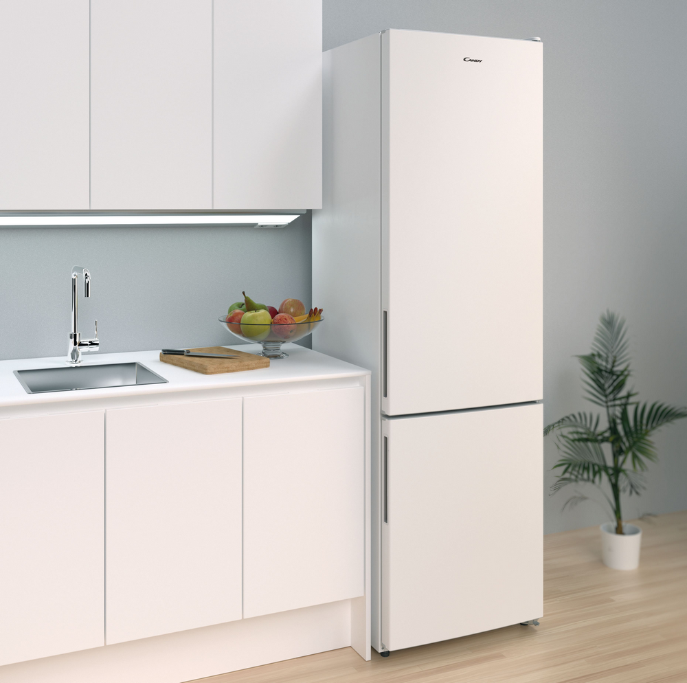 Cocina blanca con nevera, fregadero, encimera y algunas frutas.