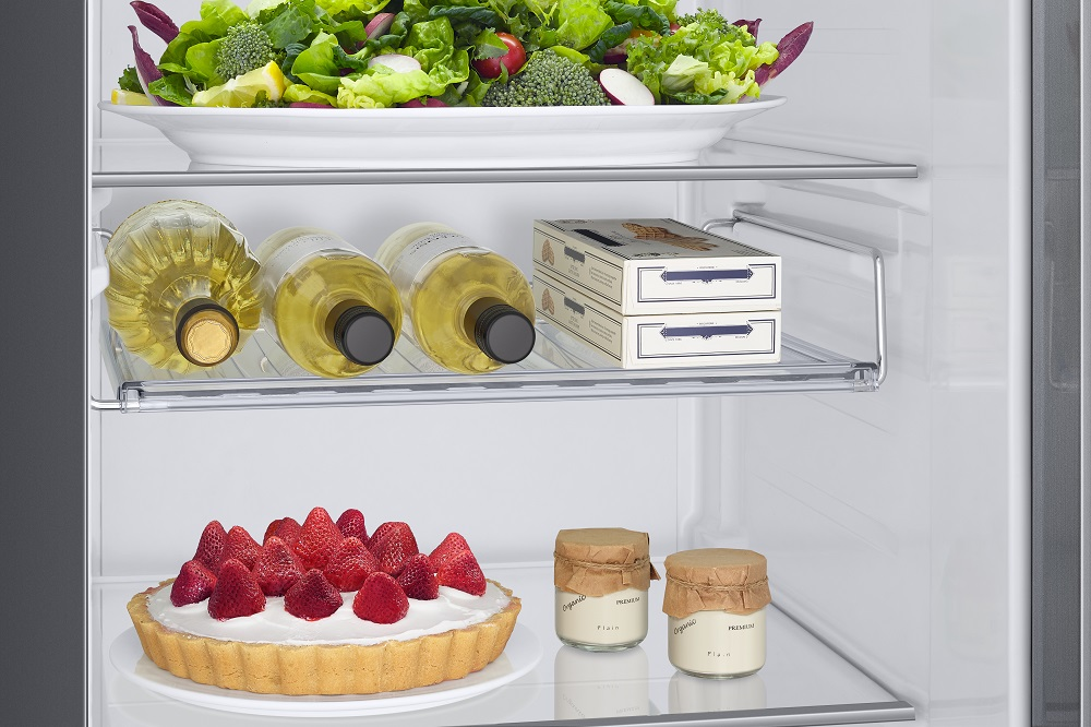Kühlschrankinnenraum. Oberes Regal: Salat, Weißweinflaschen. Unten: Erdbeerkuchen, Joghurtgläser.