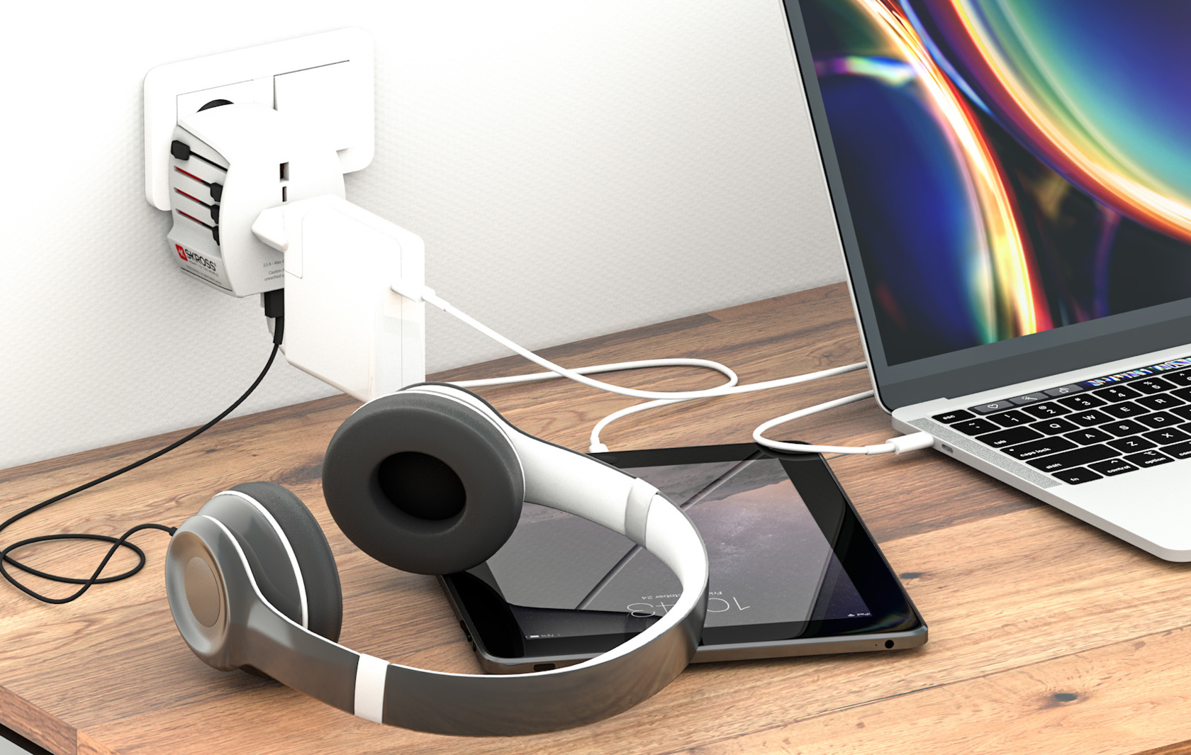Cuffie, tablet e laptop collegati a un adattatore per presa a muro.