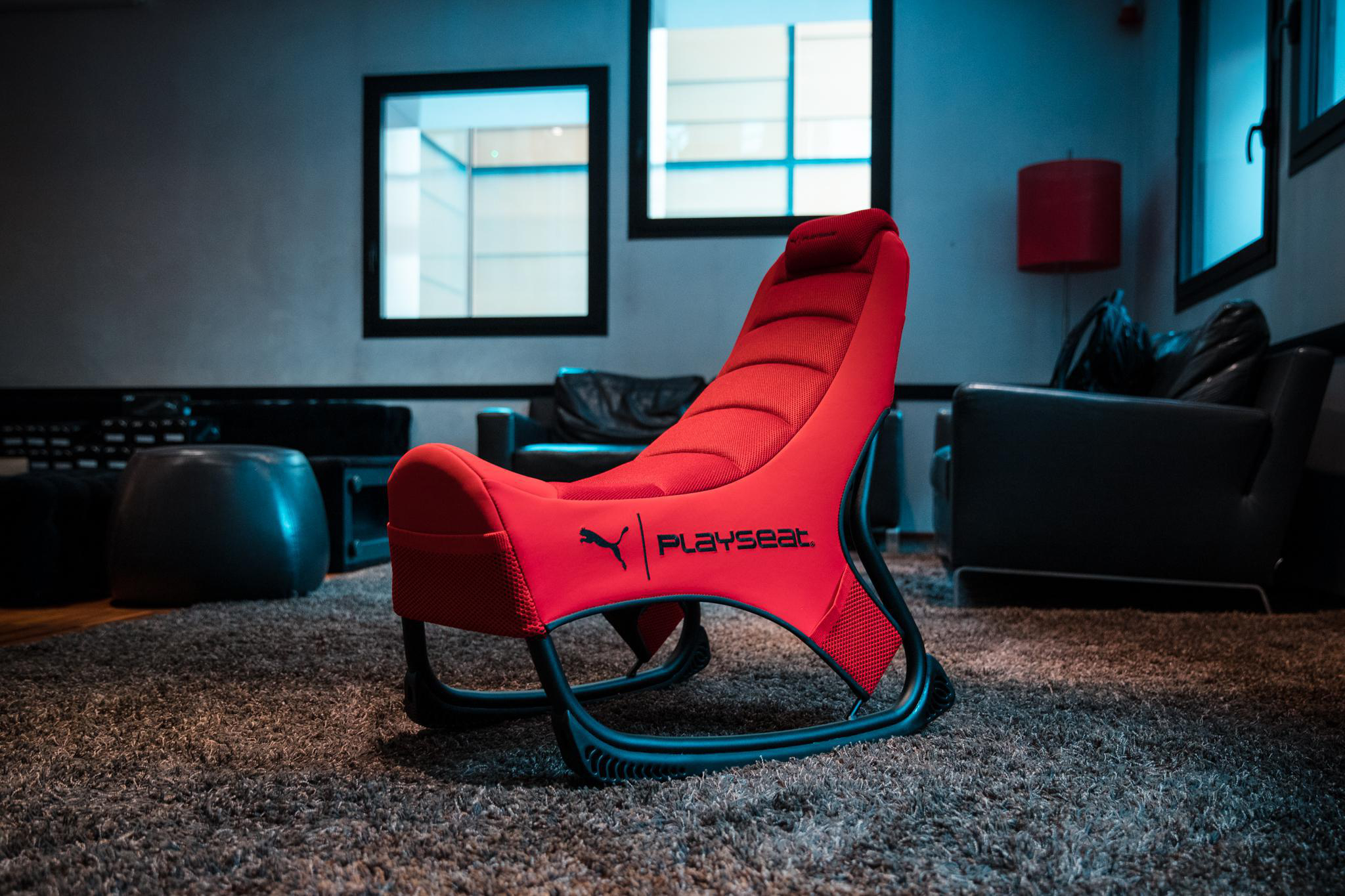 Roter Puma Playset Gaming-Stuhl in einem Raum. Der Raum hat einen grauen Teppich, schwarze Möbel und Fenster.