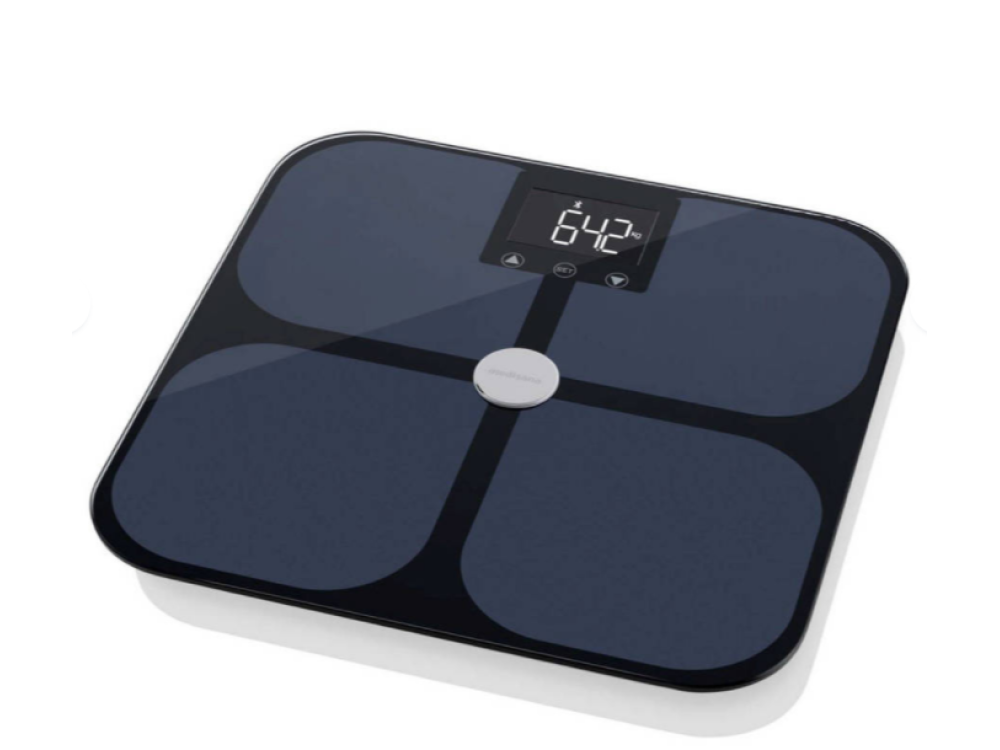 Una báscula digital negra que muestra 64.2 en la pantalla. Está sobre un fondo blanco.