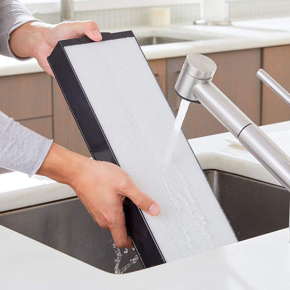 Person wäscht Luftfilter unter Wasserhahn. Der Filter ist schwarz und weiß.