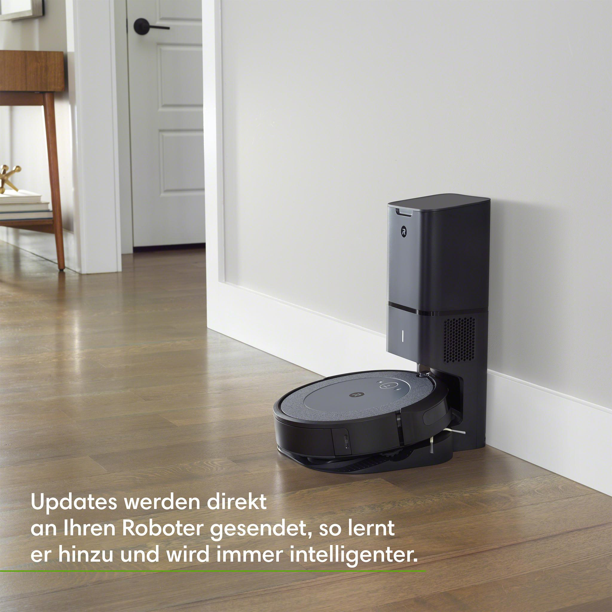 Ein schwarzer und grauer Roboter-Staubsauger auf einem Holzboden, in der Nähe seiner Ladestation.