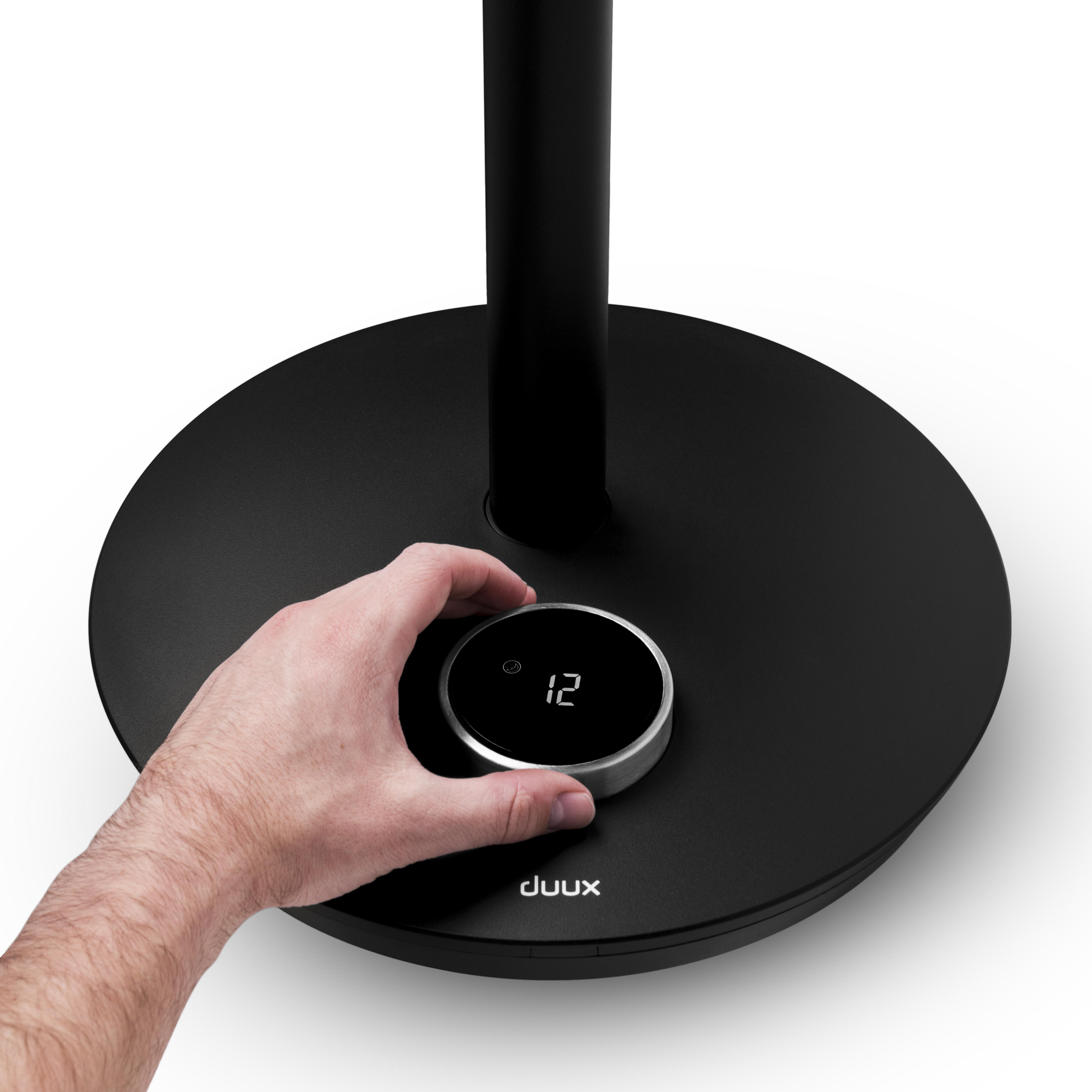 Eine Hand dreht ein Rad an einem schwarzen Lüfterfuß mit einer Digitalanzeige, die die Zahl '12' zeigt.