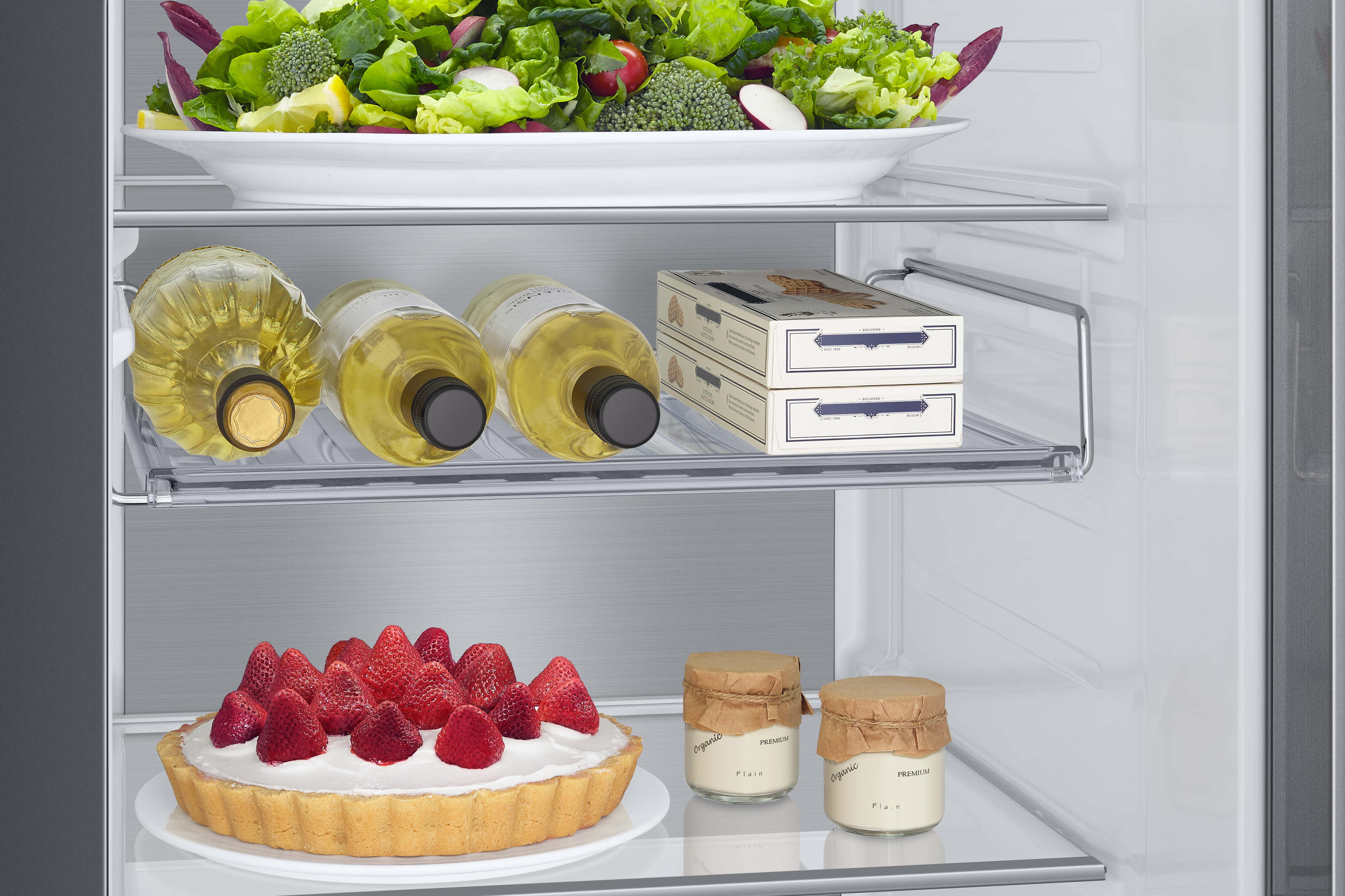 In einem Kühlschrank mit Essen auf den Regalen. Flaschen, Gebäck und Salat.