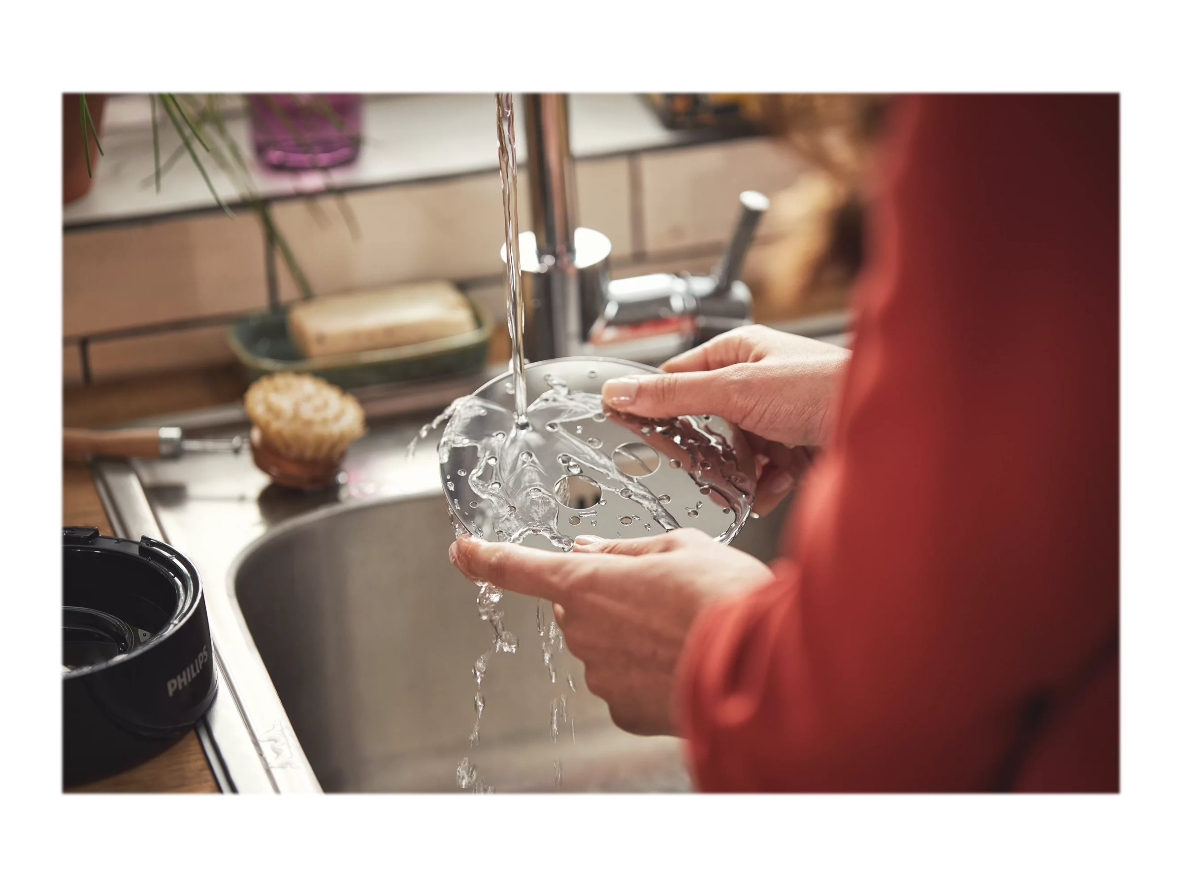 Eine Person wäscht eine Küchenmaschinenklinge unter fließendem Wasser im Waschbecken.