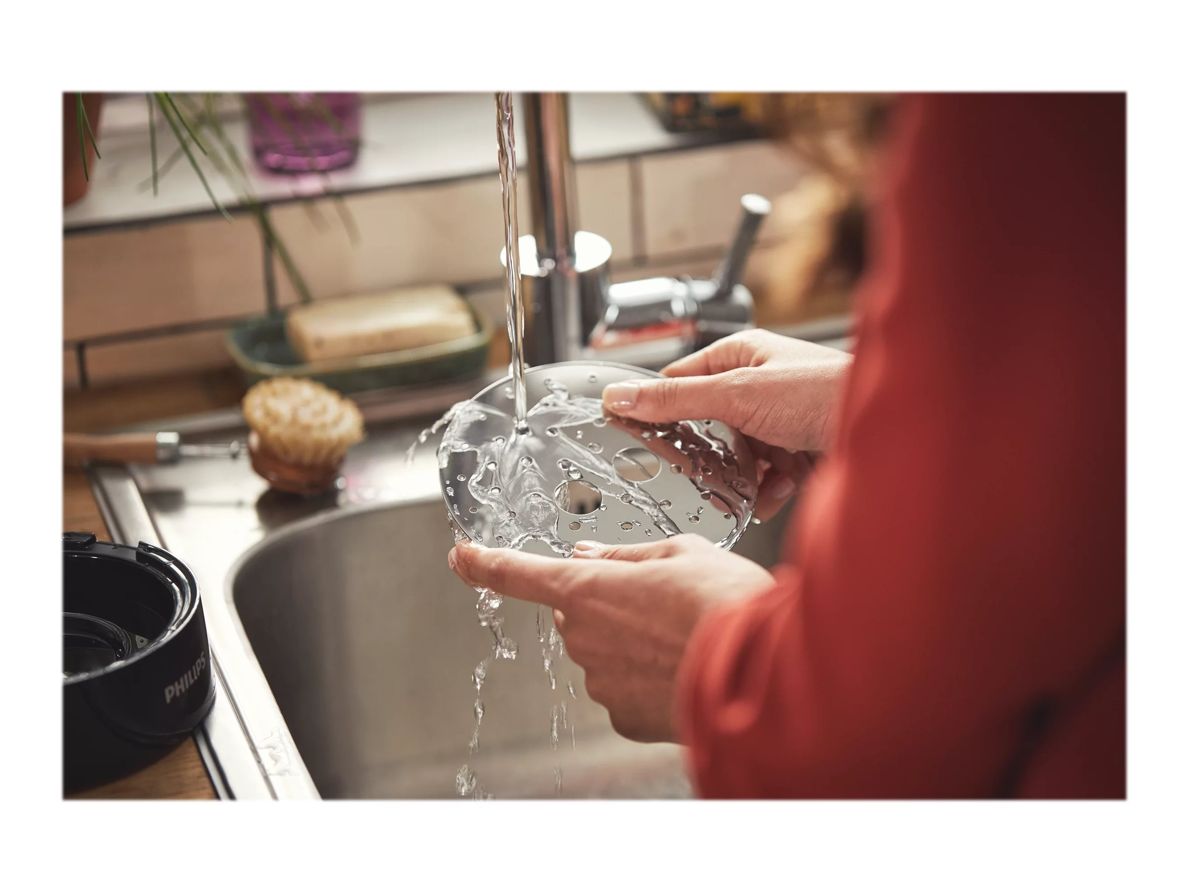 Hände waschen ein Küchenmaschinenmesser unter fließendem Wasser im Waschbecken.