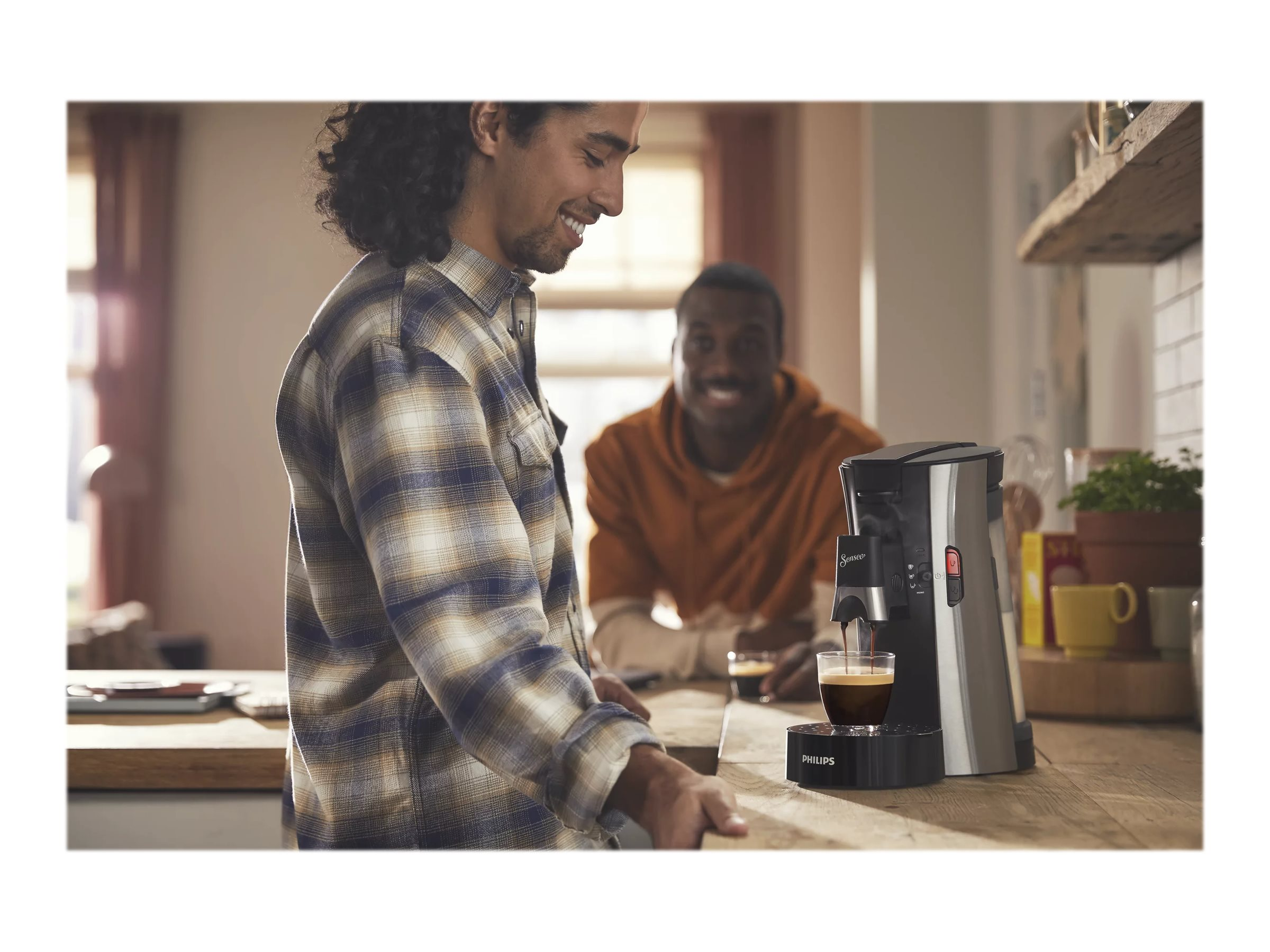 Eine Person, die Kaffee mit einer Kaffeemaschine zubereitet, eine andere Person schaut zu.