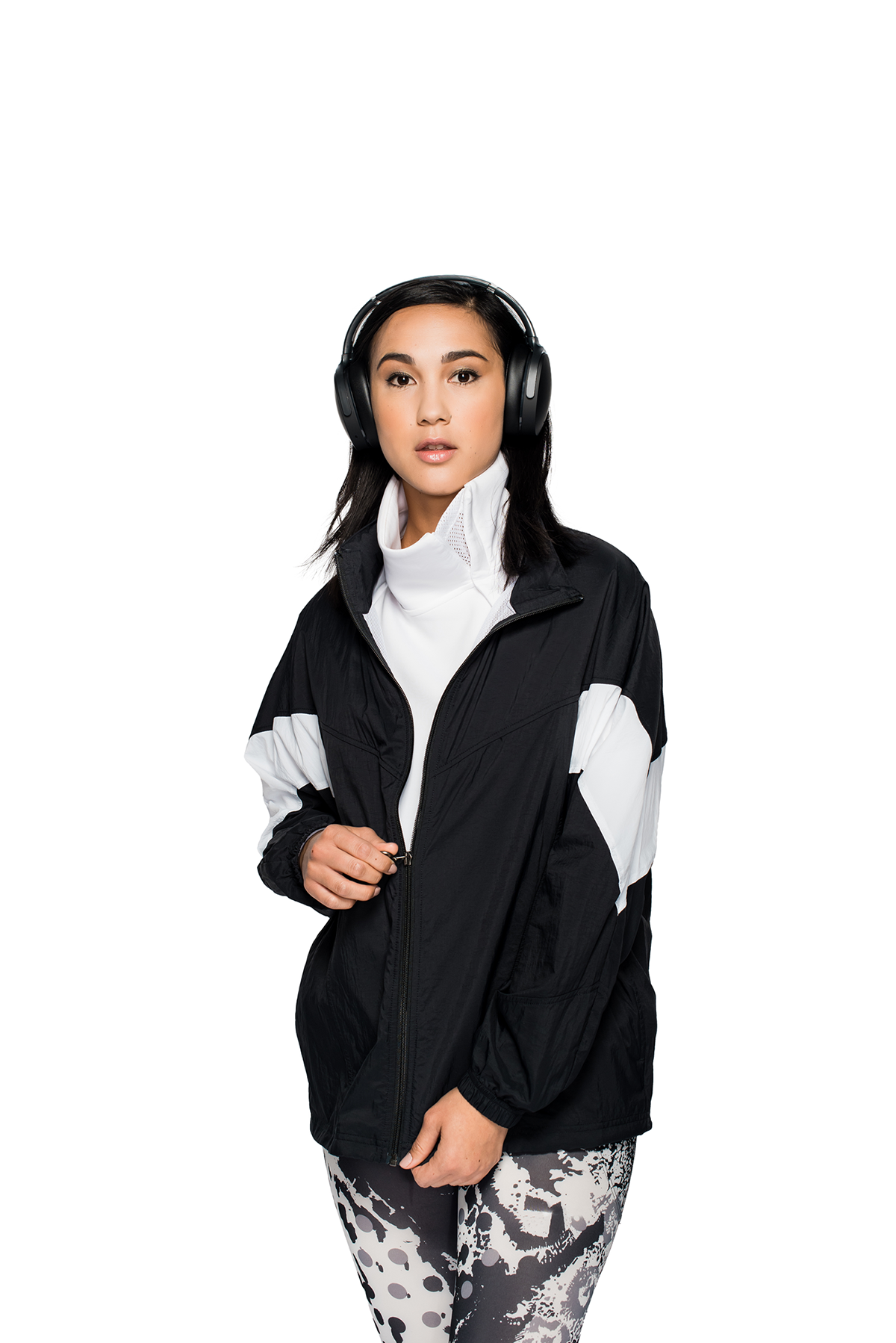 Woman in a jacket and leggings wearing headphones. Posing against a white background.