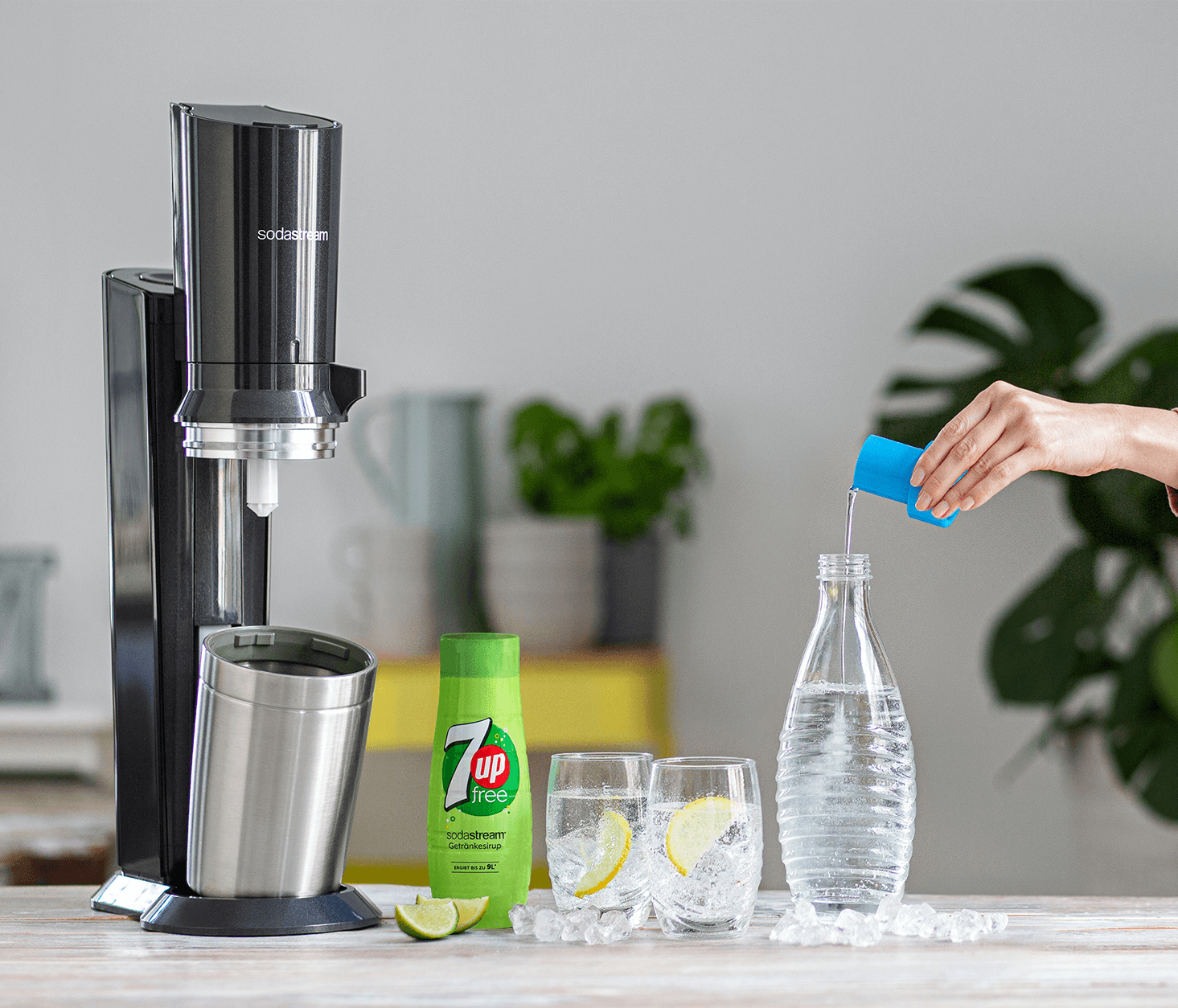 Schwarzer SodaStream, Soda, 7up-Flasche, zwei Gläser mit Zitrone, Eis und eine Hand, die Soda einschenkt.