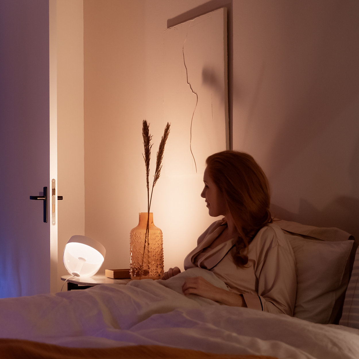 Frau im Bett, Lampe auf einem Tisch, Stillleben an der Wand.
