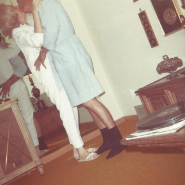 Paar küsst sich, einer in Weiß, einer in Blau, in einem Raum mit Möbeln.