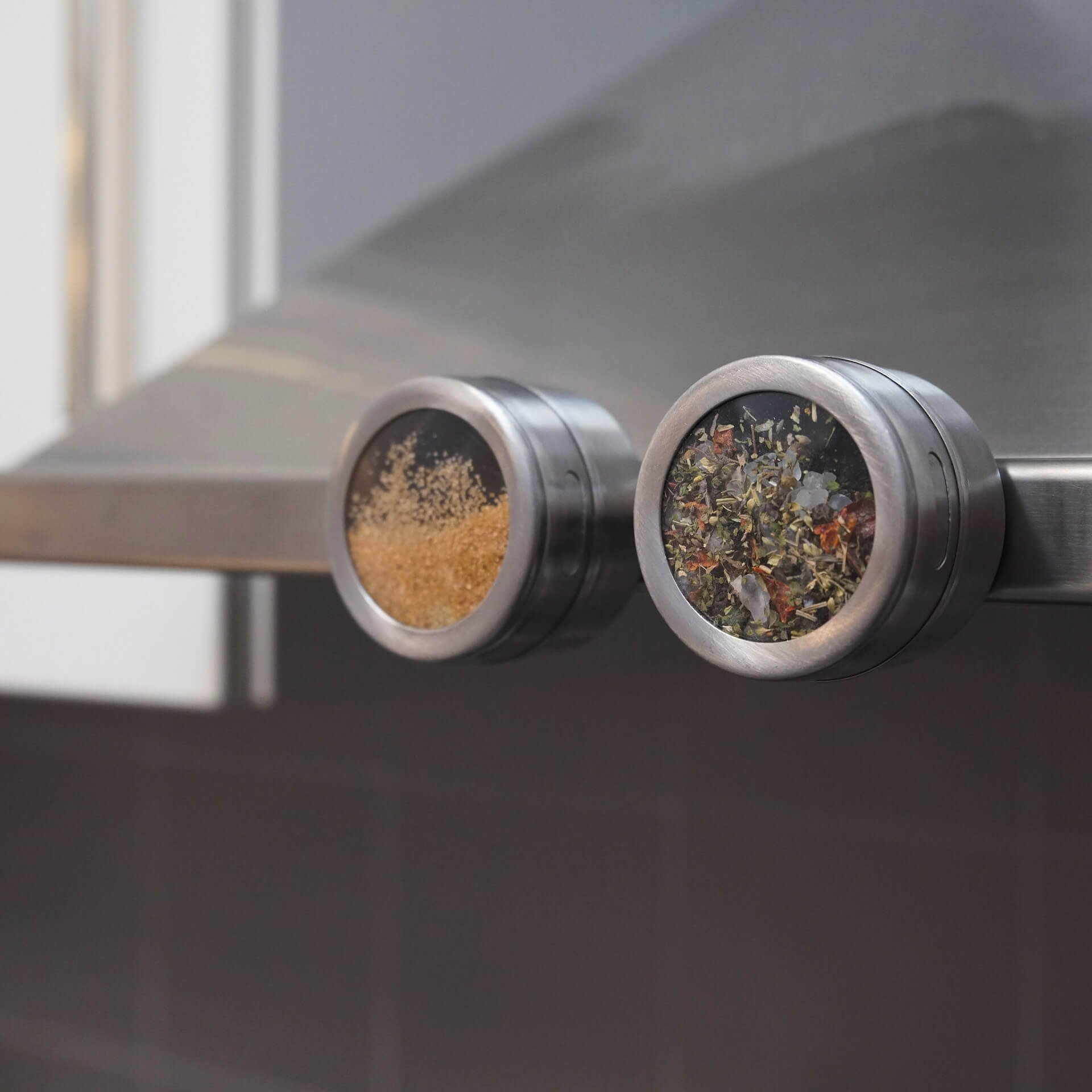Gewürzregale aus Edelstahl mit zwei runden Behältern, gefüllt mit Gewürzen, auf Metalloberfläche.
