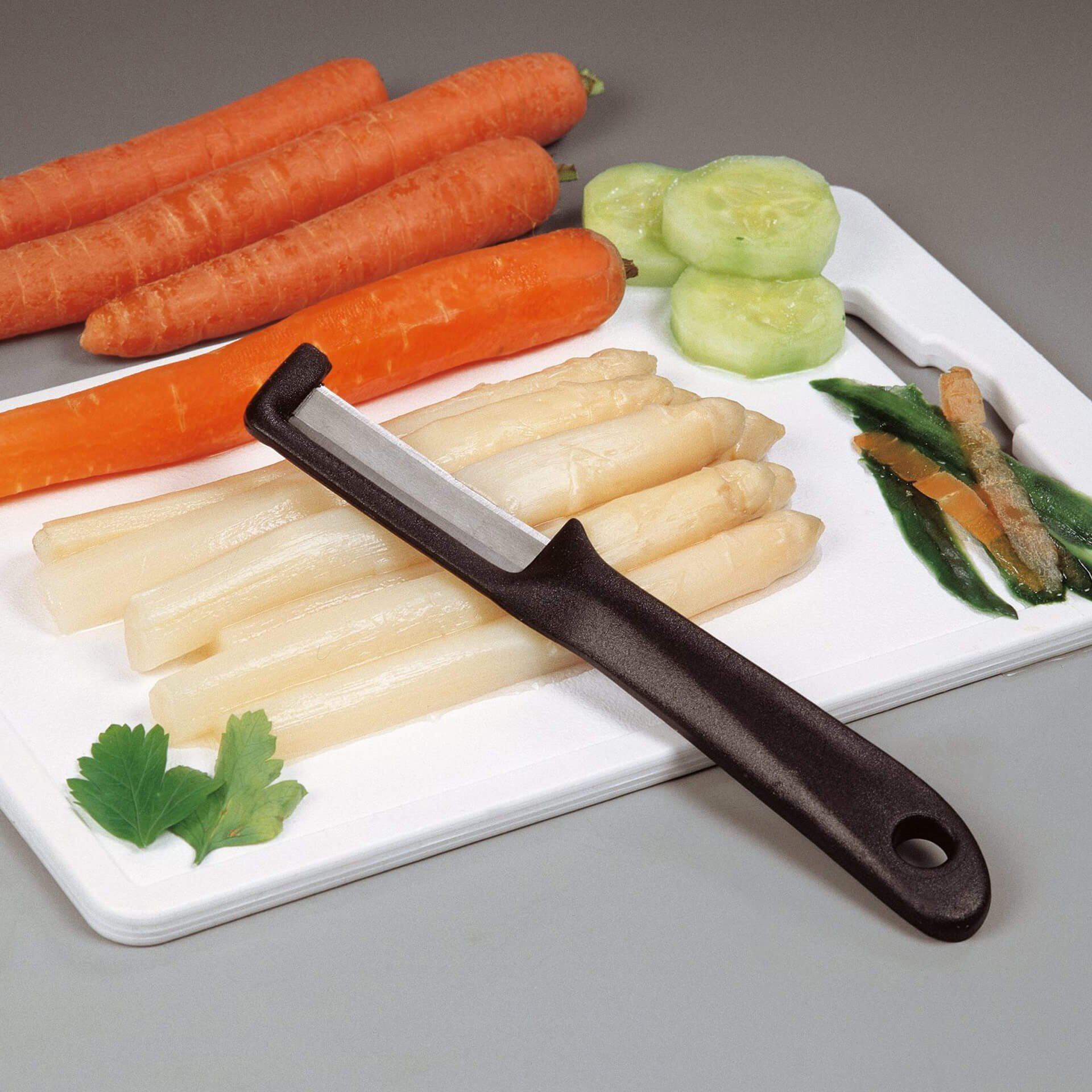 Schneidebrett mit Karotten, Spargel, Gurkenscheiben und einem Sparschäler.
