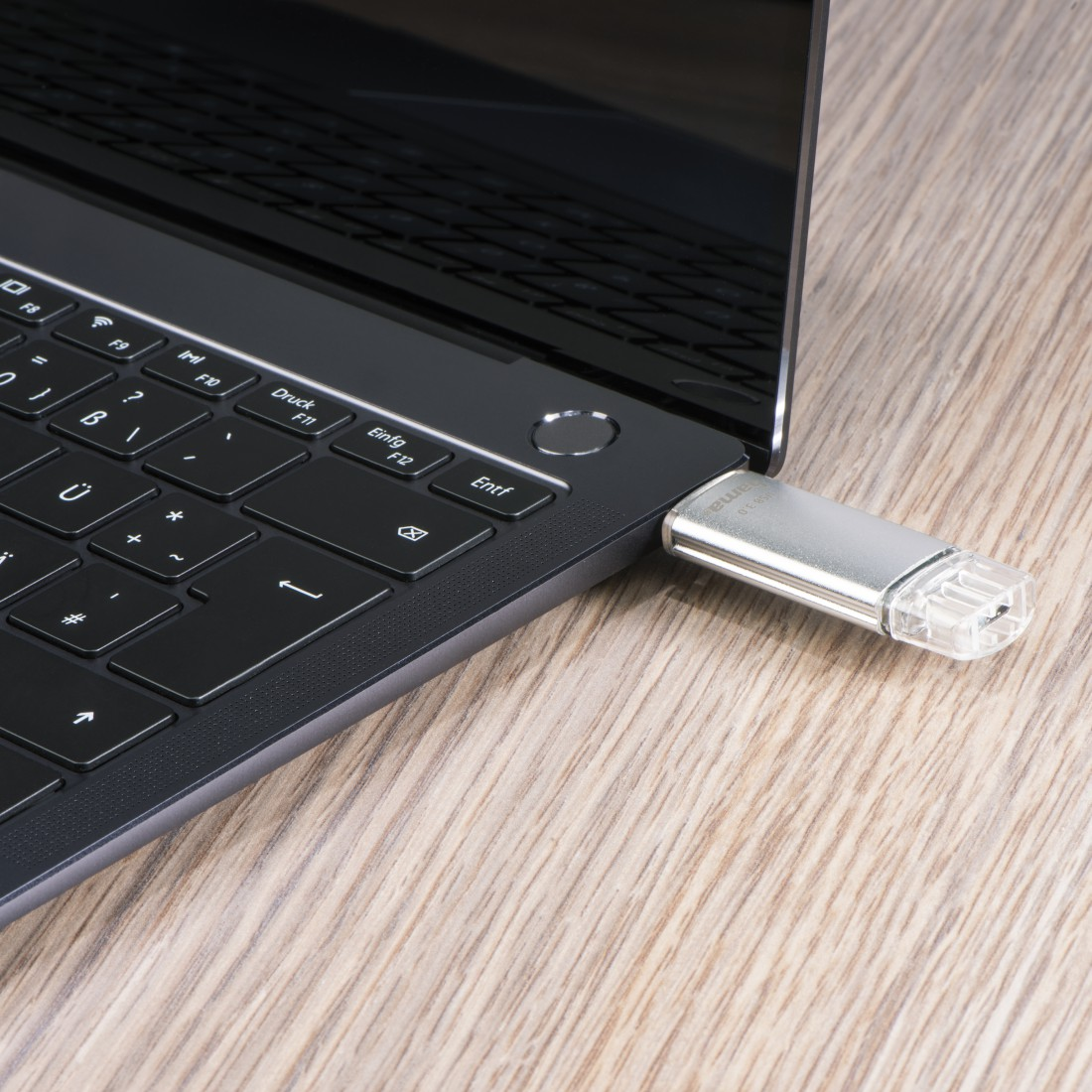 Ein silberner USB-Stick ist in einen schwarzen Laptop auf einem Holzschreibtisch gesteckt.