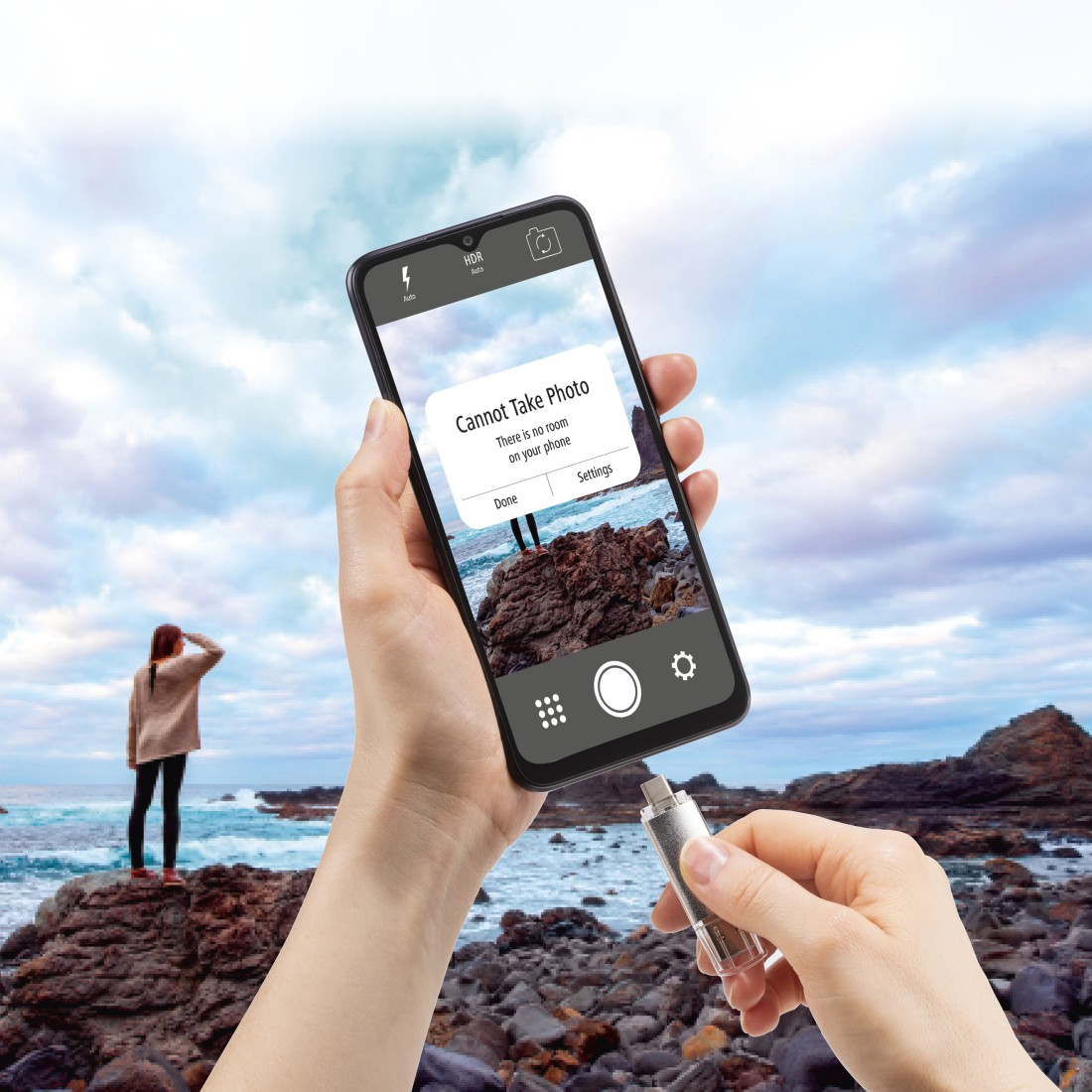 Hand hält Telefon mit Foto und USB. Hintergrund: Ozean, Felsen und Himmel.