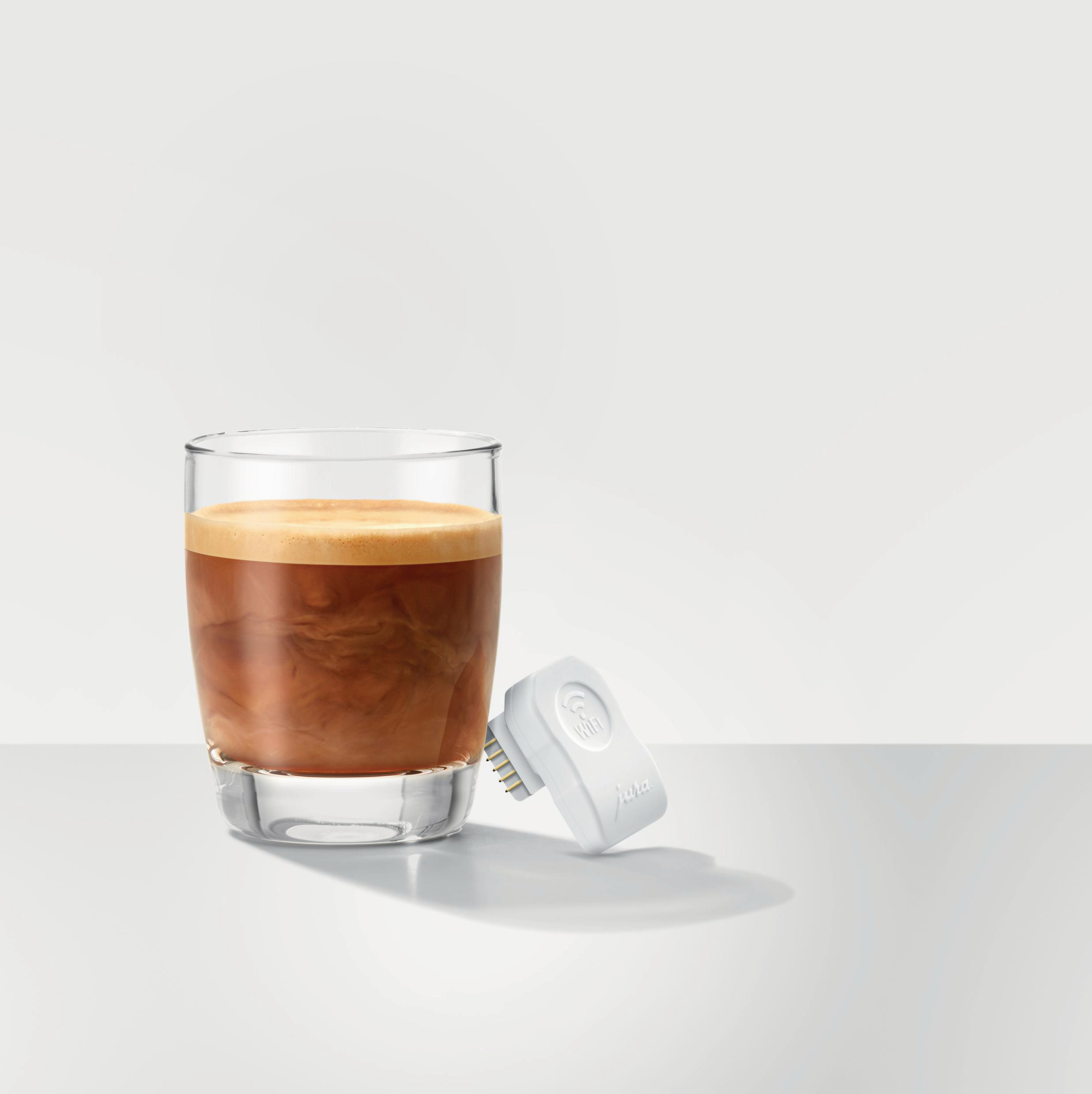 Glas Kaffee mit Sahne neben einem weißen, kleinen JURA-WLAN-Anschluss.