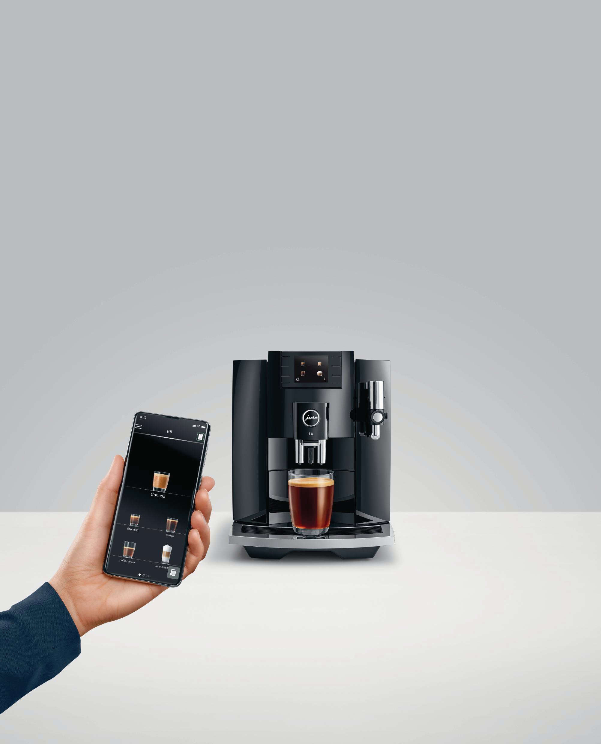 Eine Kaffeemaschine mit einem Glas Kaffee. Eine Hand hält ein Telefon mit Kaffeeoptionen.