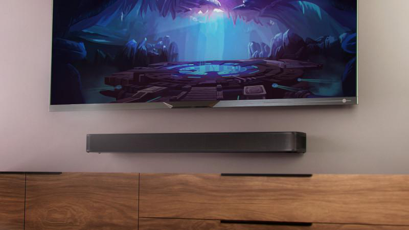 TV und Soundbar an der Wand. Bildschirm zeigt eine Höhlenszene. Holzschrank unter der Soundbar.