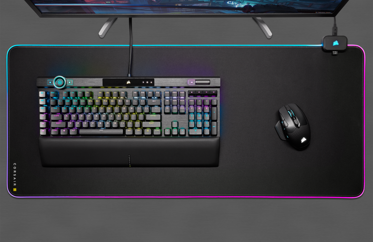 Un clavier, une souris et un tapis de souris noirs avec éclairage RVB. Un moniteur est au-dessus.