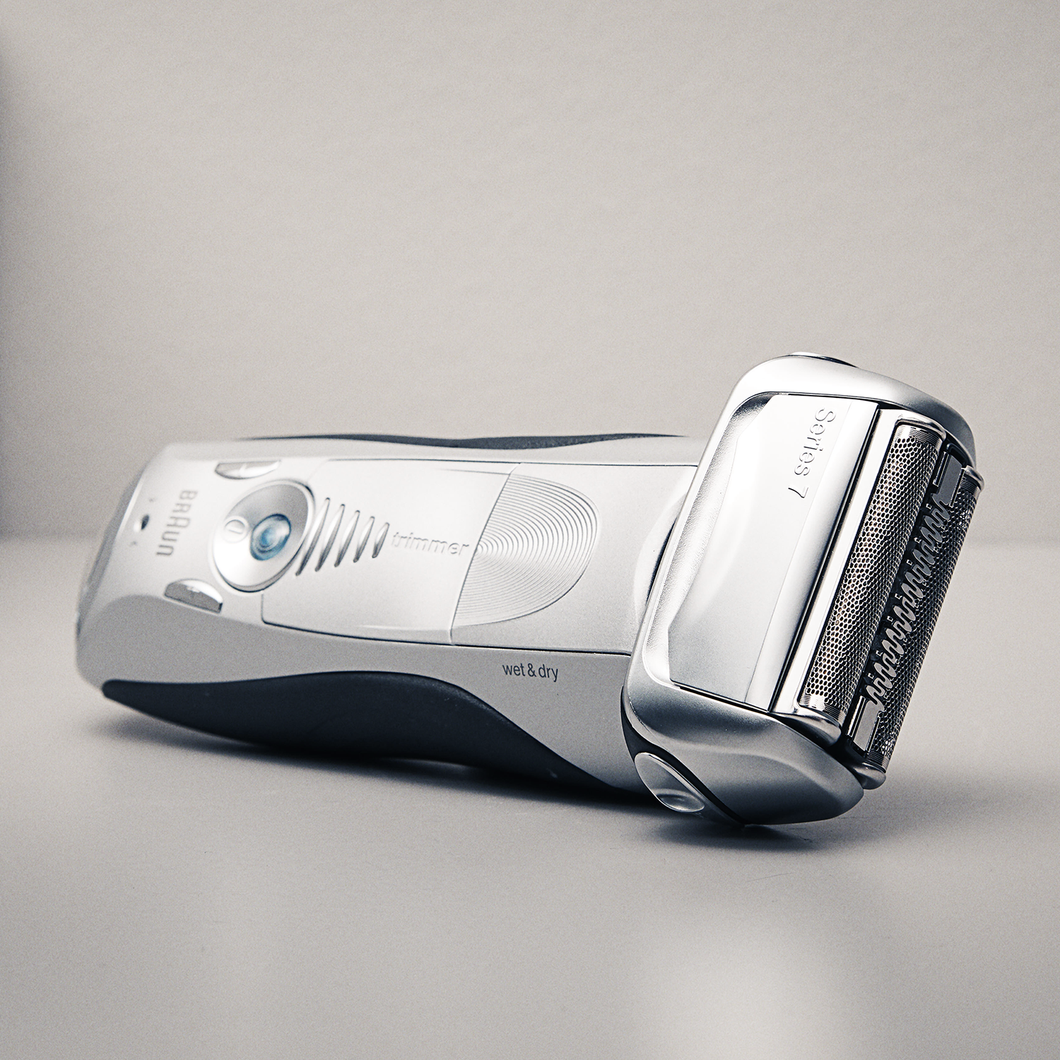 Silver and black electric shaver. It is on a white surface. The background is light gray.