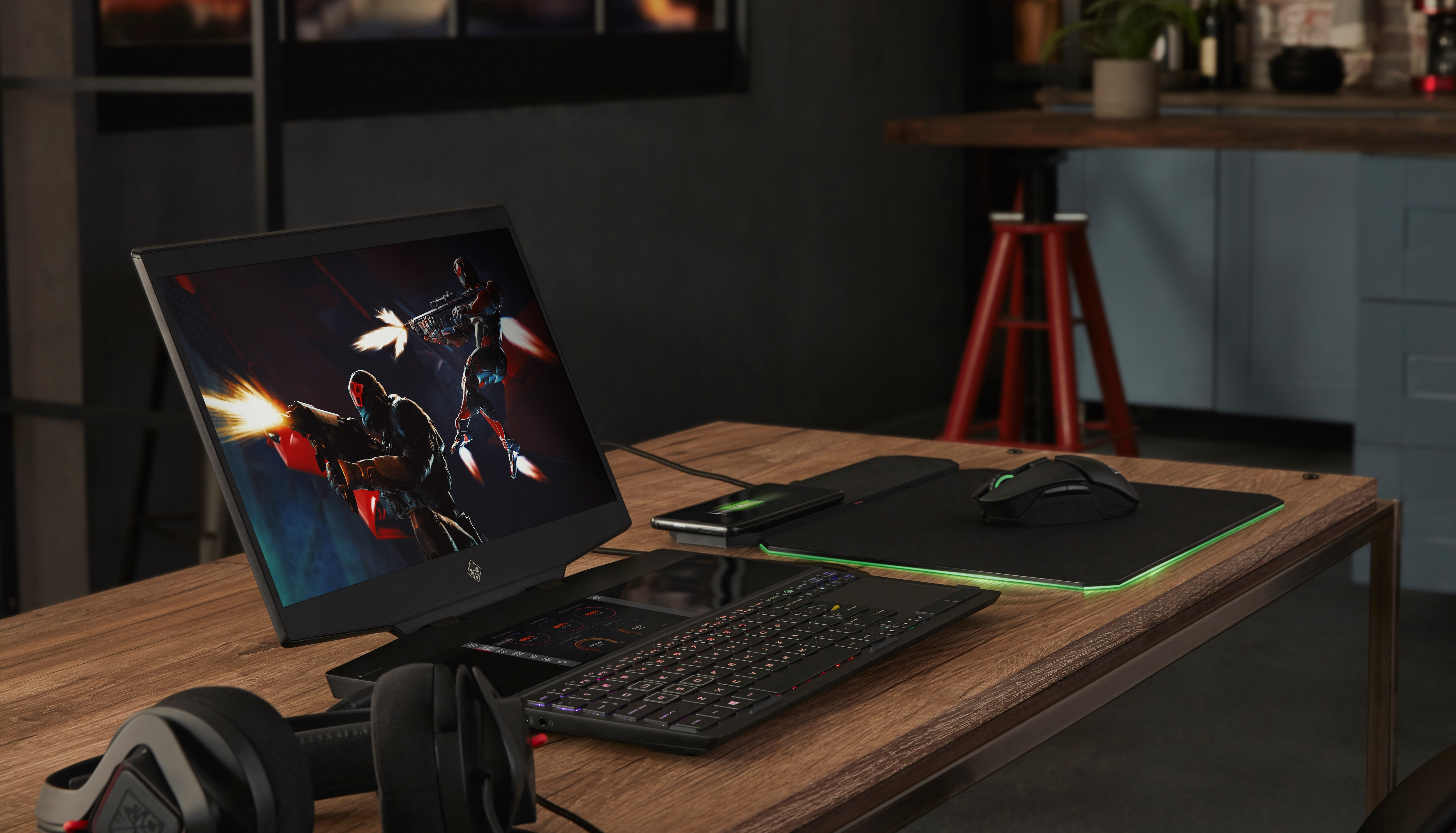 Una computadora portátil para juegos con un juego que se muestra en la pantalla, con accesorios para juegos en un escritorio.