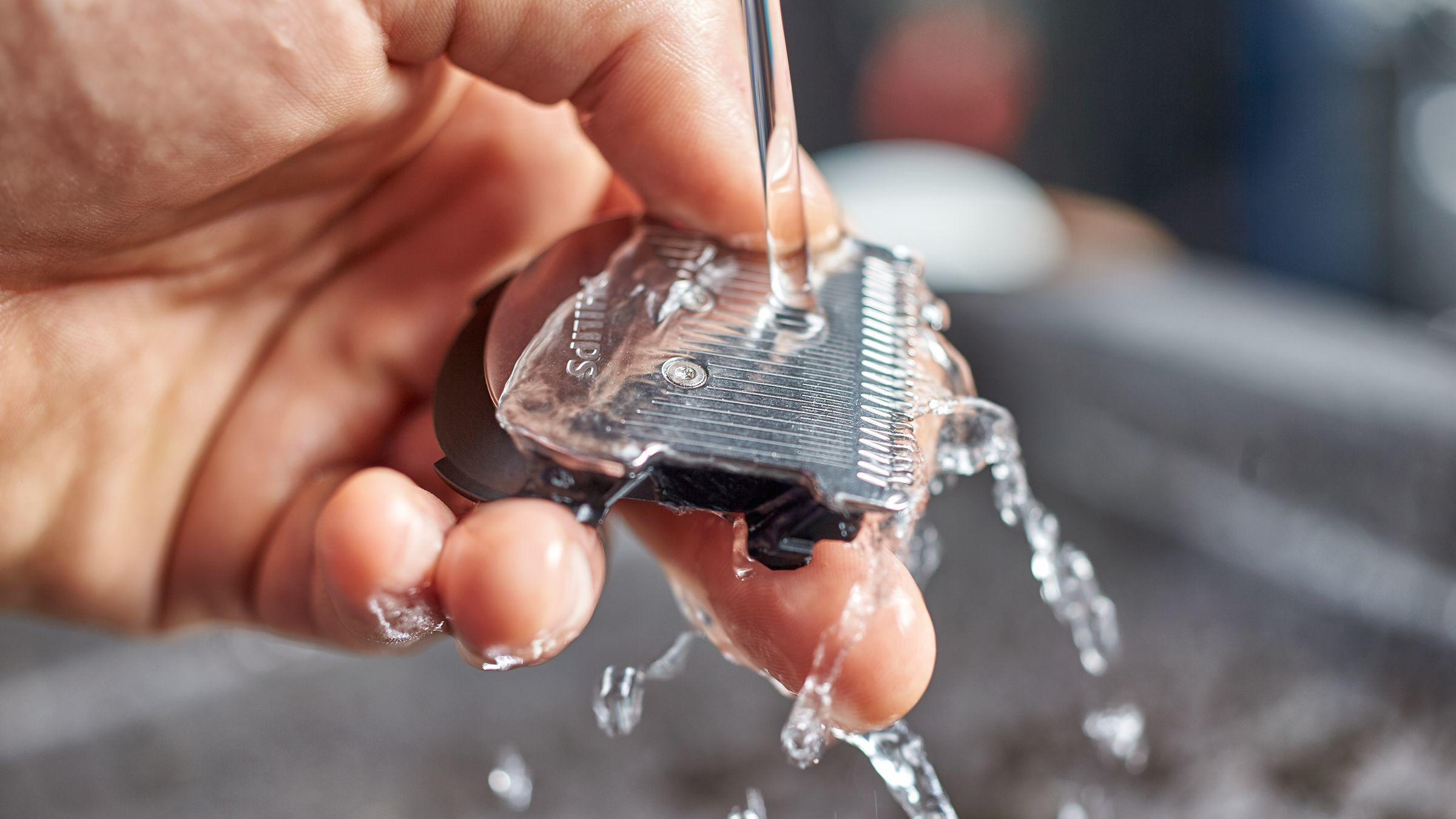 Una mano sosteniendo un cabezal de afeitado Philips bajo agua corriente, limpiando el dispositivo.
